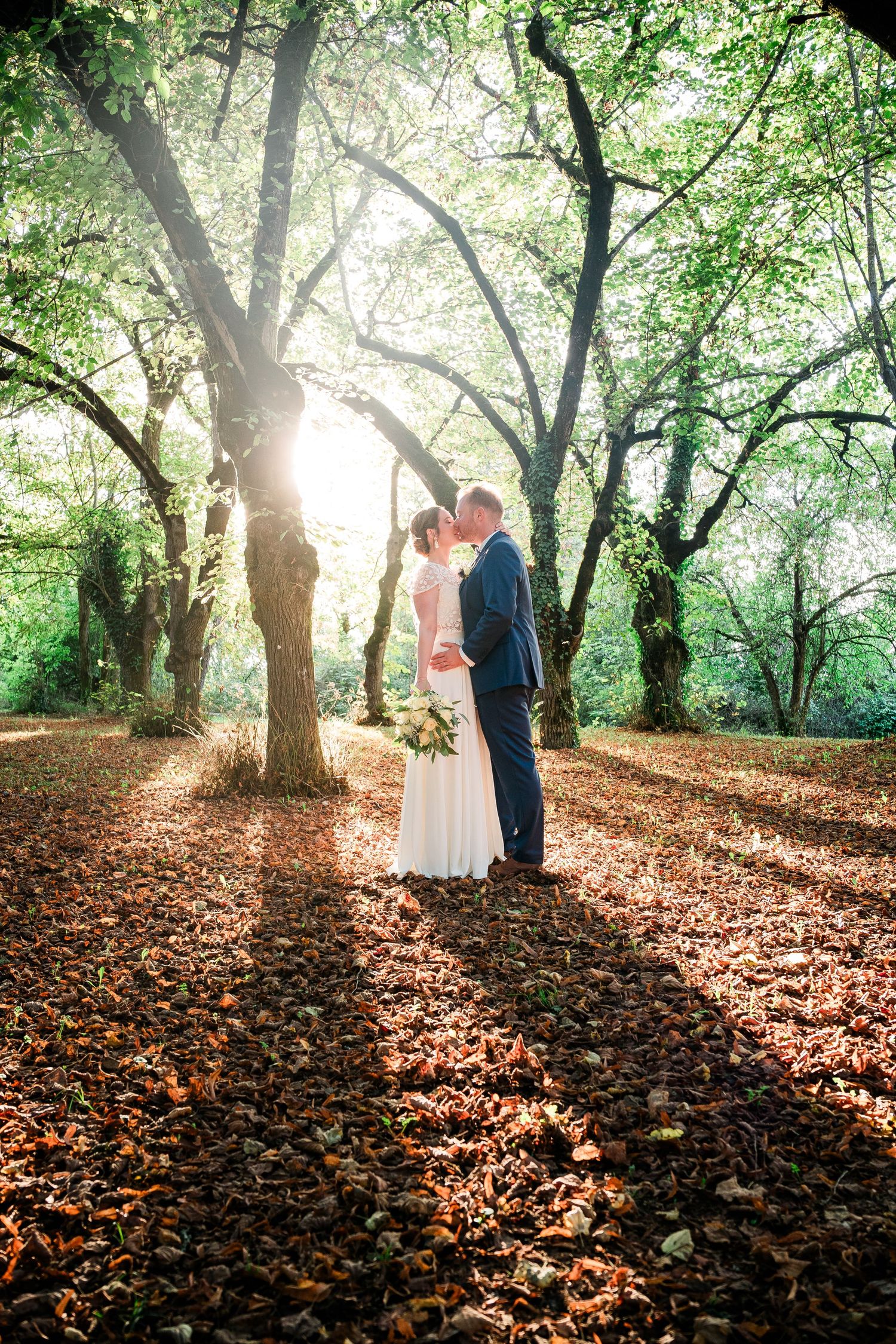 Romantic wedding portraits in a wooded area with sunlight filtering through autumn leaves.