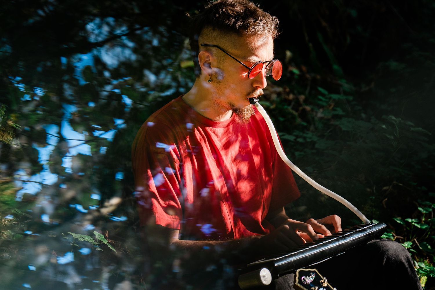 Person in red shirt and sunglasses reading in dappled sunlight outdoors.