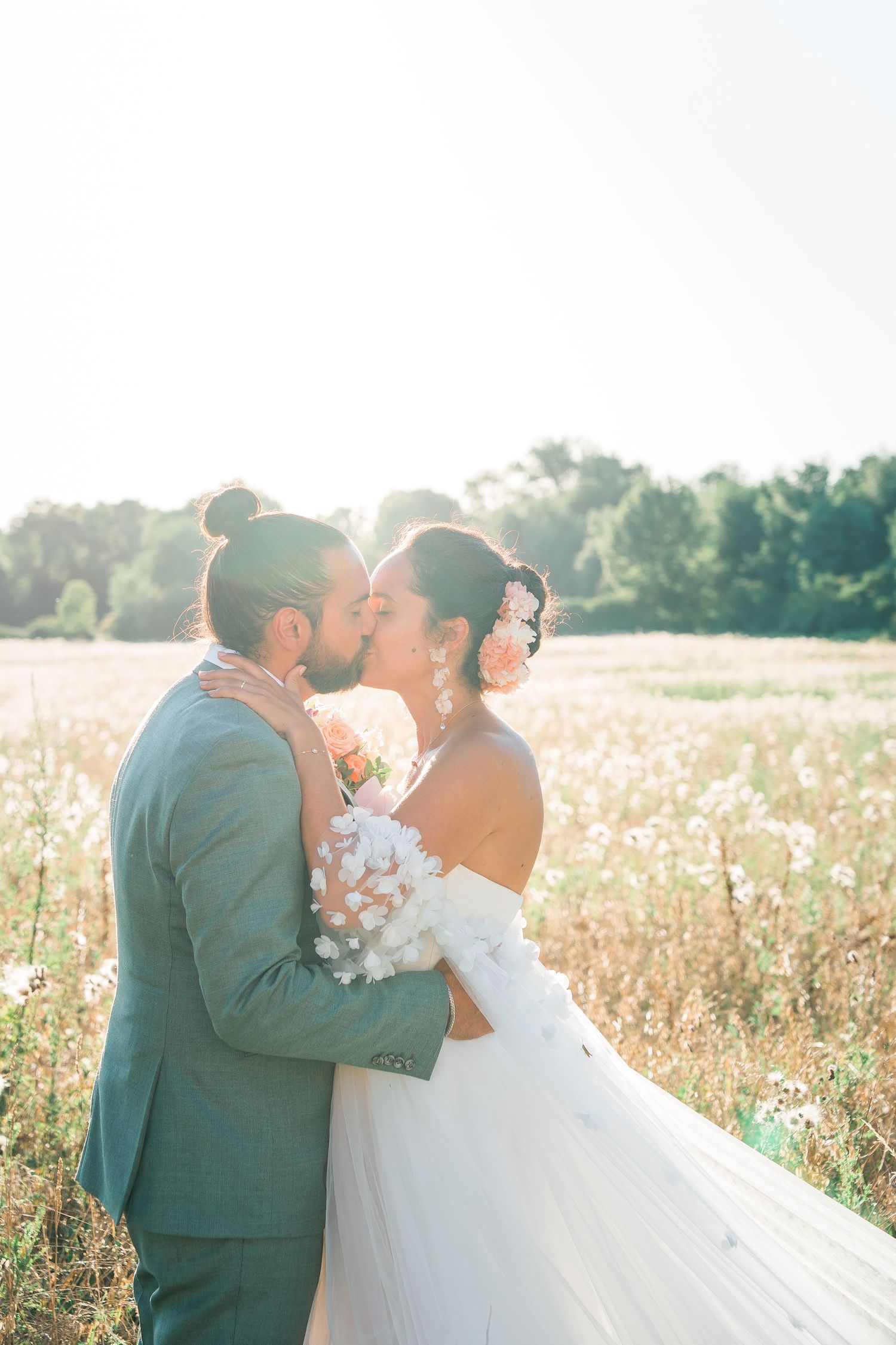 A romantic wedding photoshoot in a sunlit field with the couple embracing.