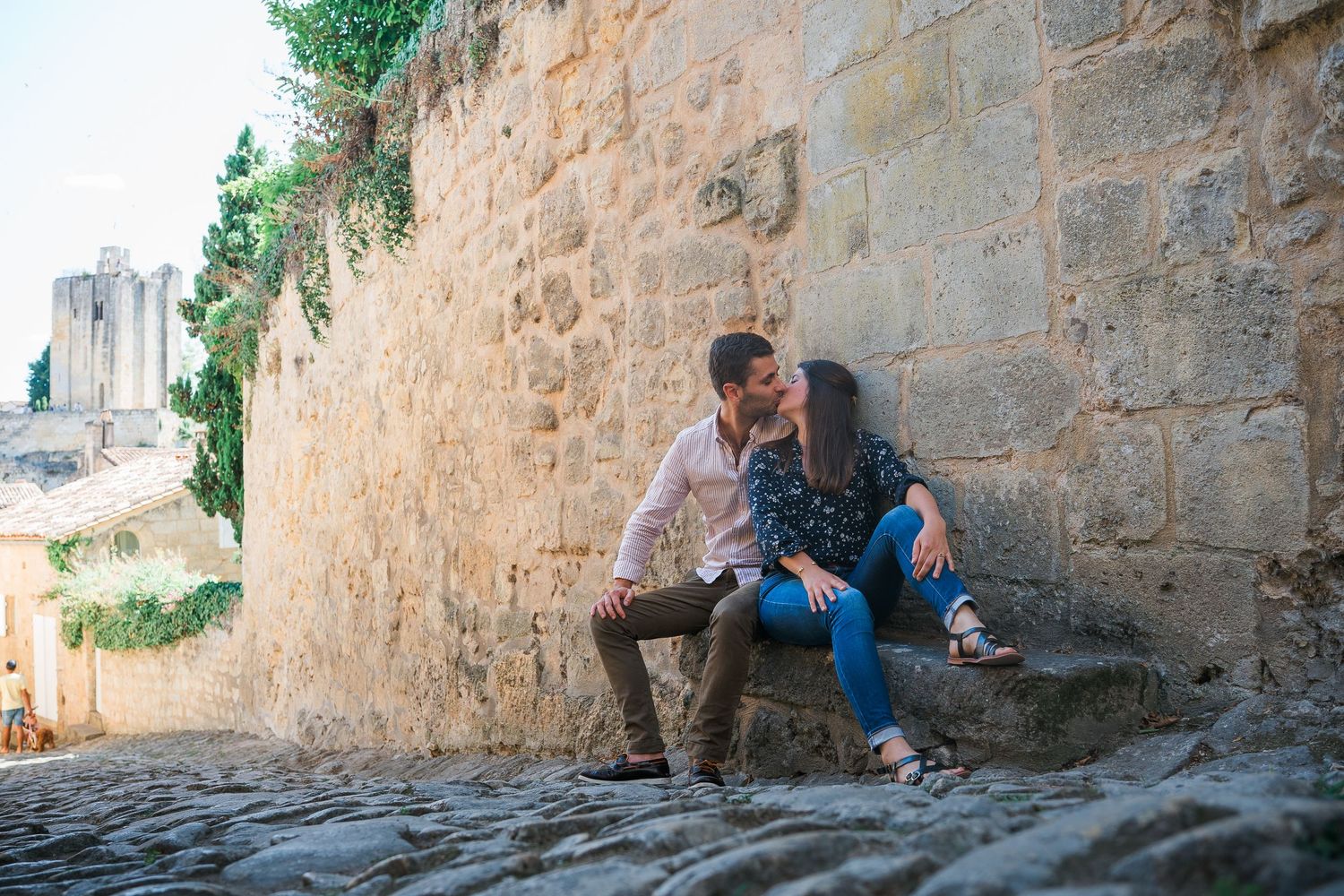 Couple sitting together on stone steps against ancient wall architecture.