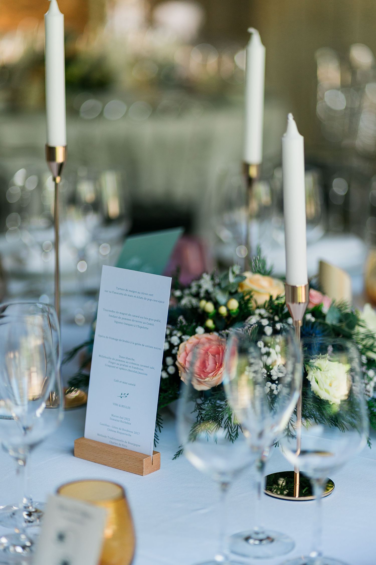 Elegant wedding table setting with white candles, roses, and menu cards on a crisp white tablecloth.