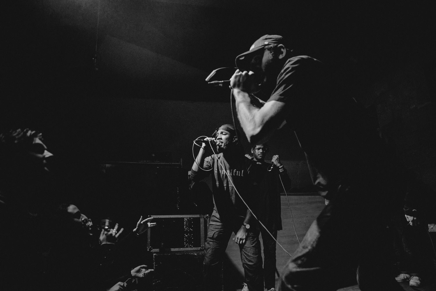Black and white concert photo of performers on stage during a dramatic performance with dramatic lighting and poses.