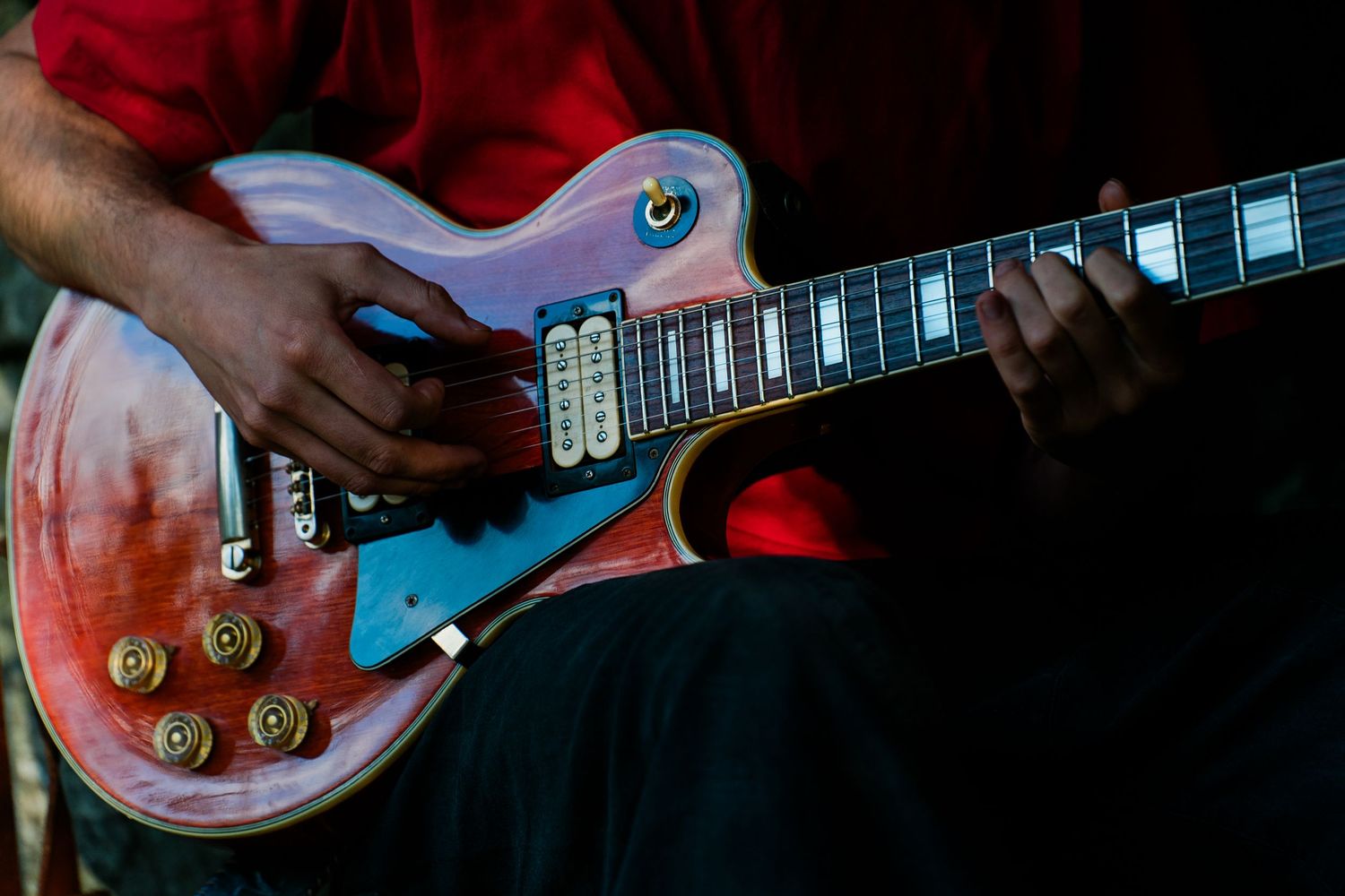 Close-up view of hands playing a red electric guitar with chrome hardware and black pickguard.