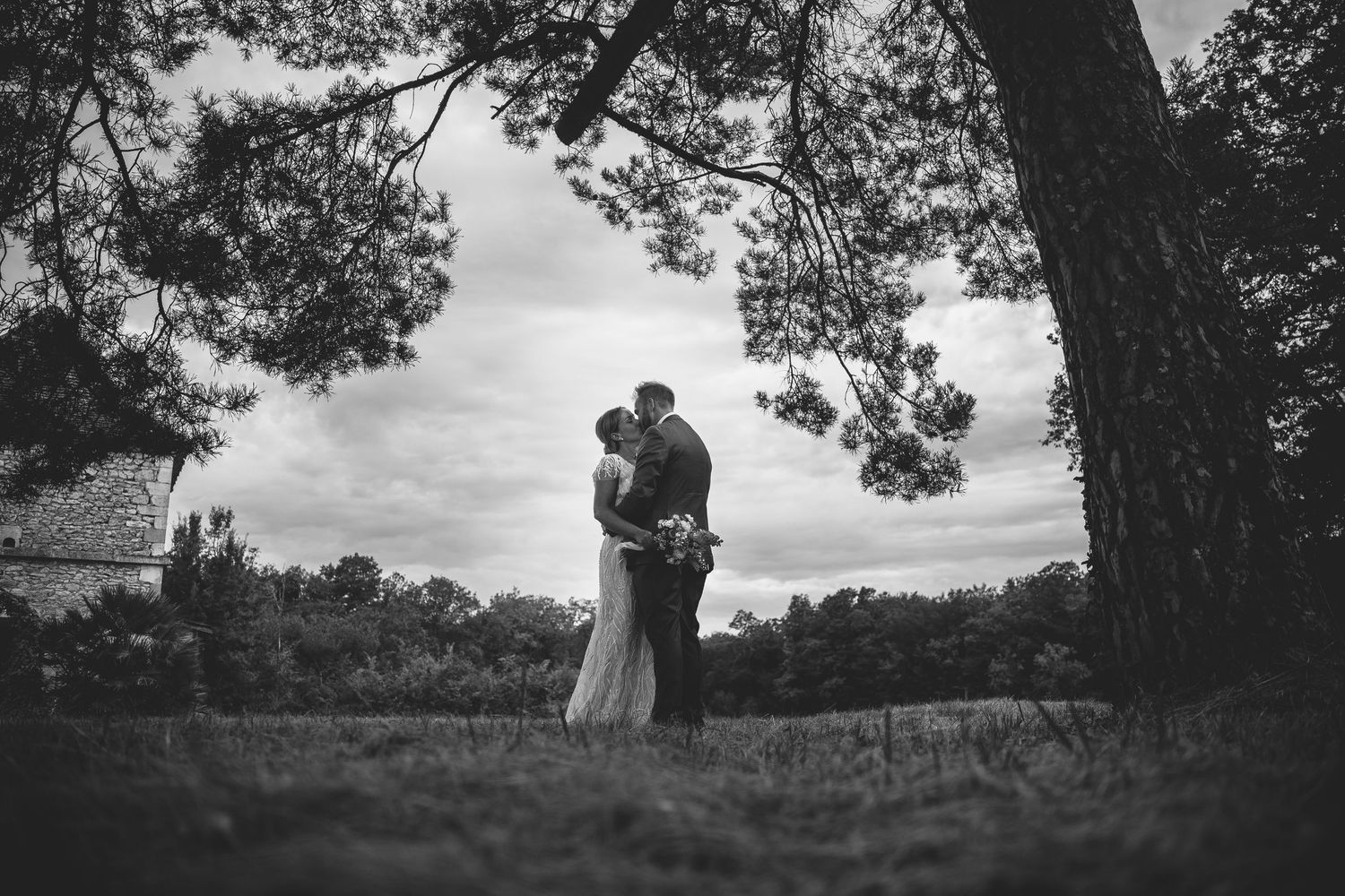 Silhouetted couple stands together against dramatic cloudy sky in natural outdoor setting.