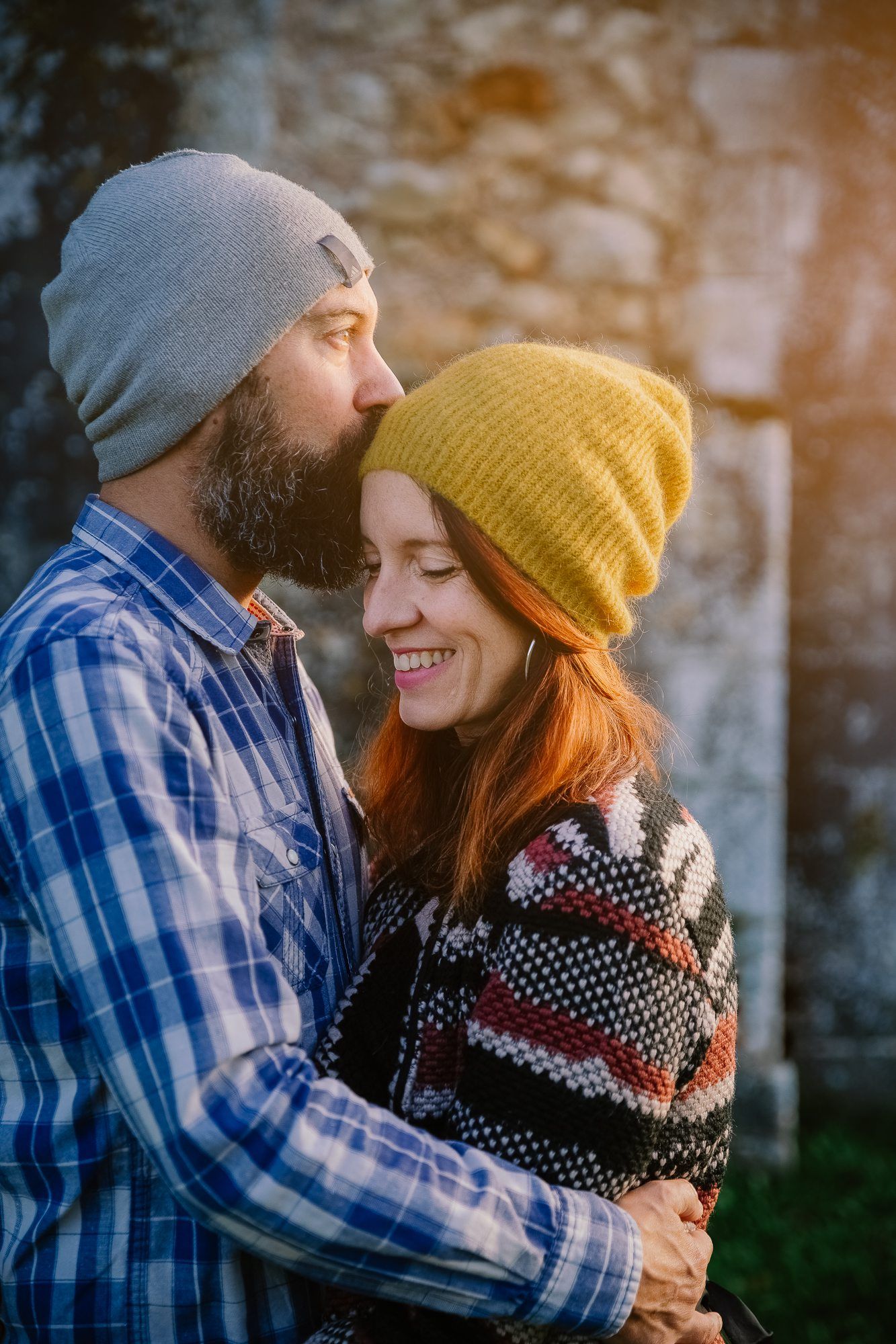 Cozy winter couple in knit beanies and plaid share warm embrace outdoors.