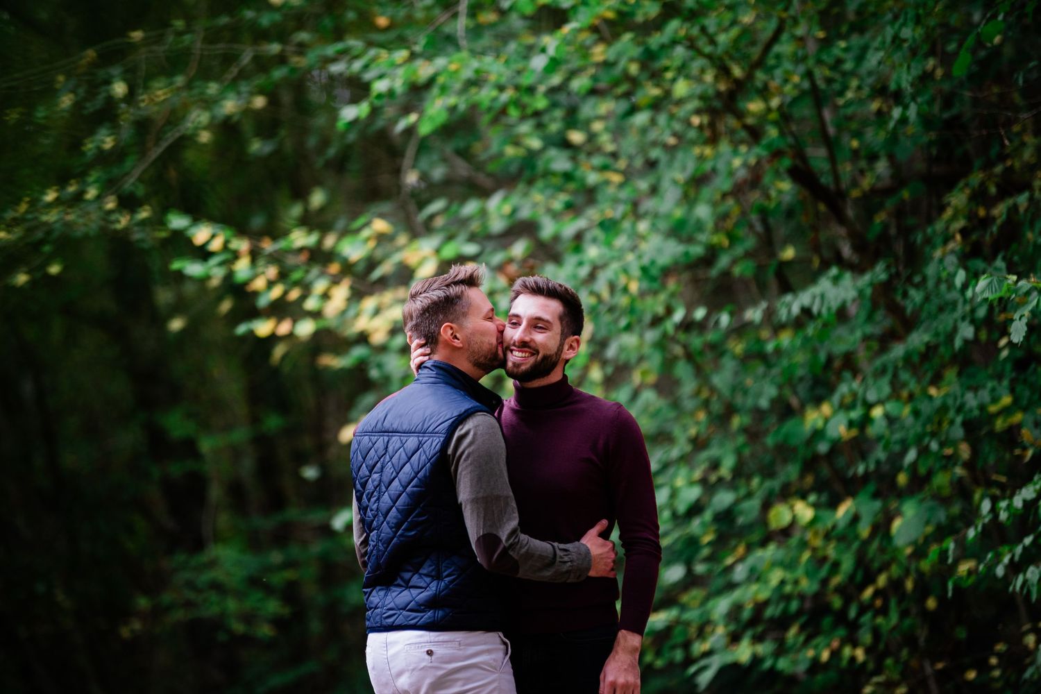 A couple embraces in a romantic outdoor setting surrounded by lush green foliage.