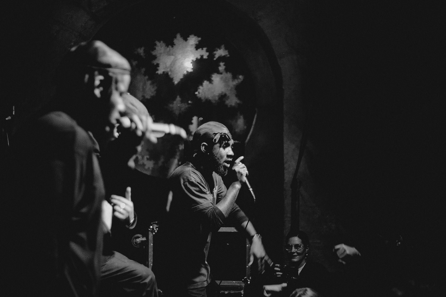 Black and white photo of performers on stage during a musical performance with dramatic lighting and smoke effects.