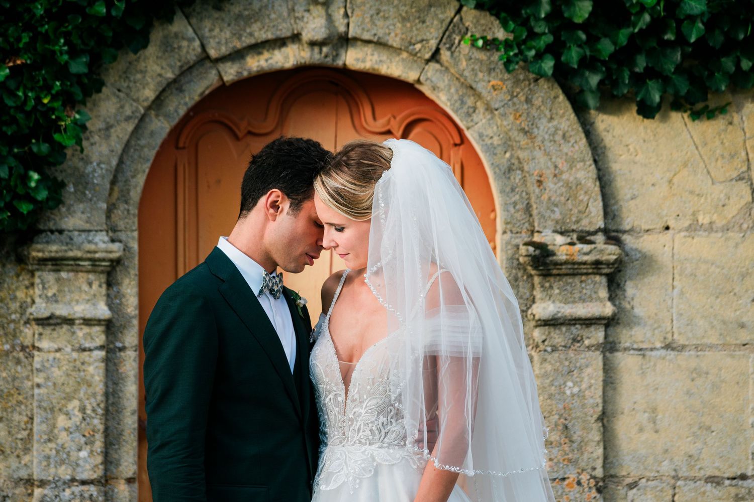 Romantic wedding moment captured under a stone archway with soft natural lighting.