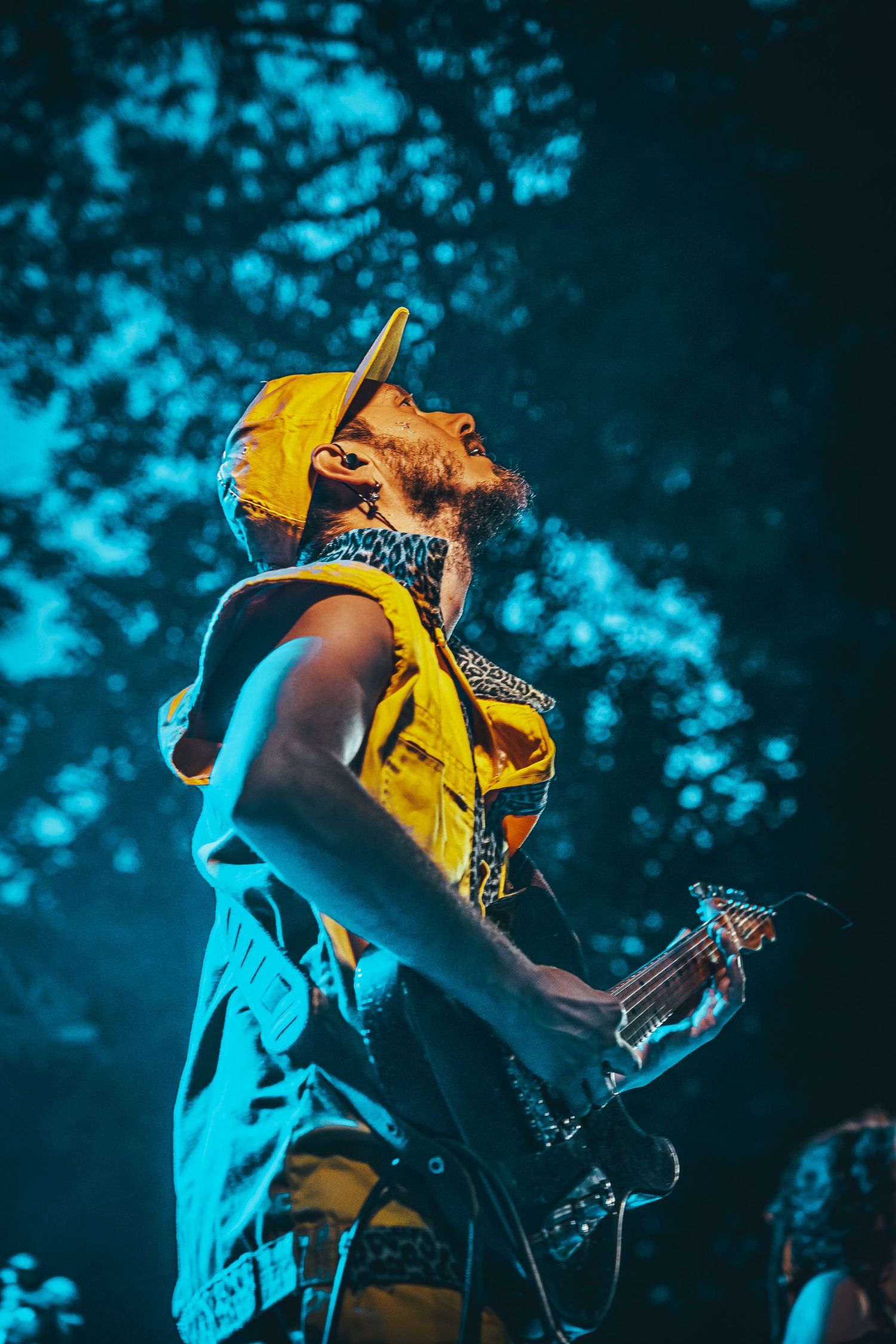 Musician in yellow shirt performs energetically on stage under dramatic blue lighting during a concert performance.