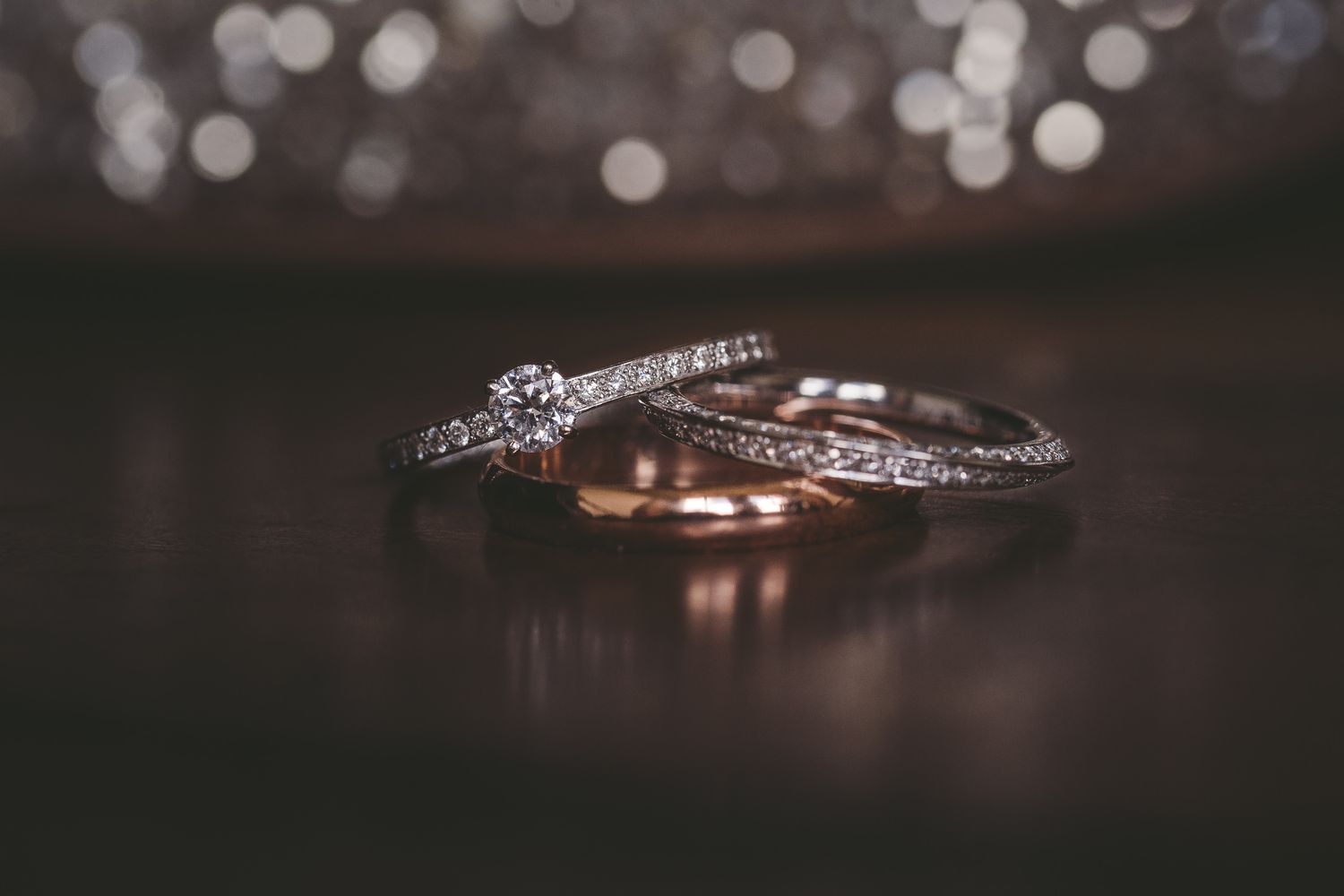 Elegant wedding bands and engagement ring photographed with soft bokeh background.