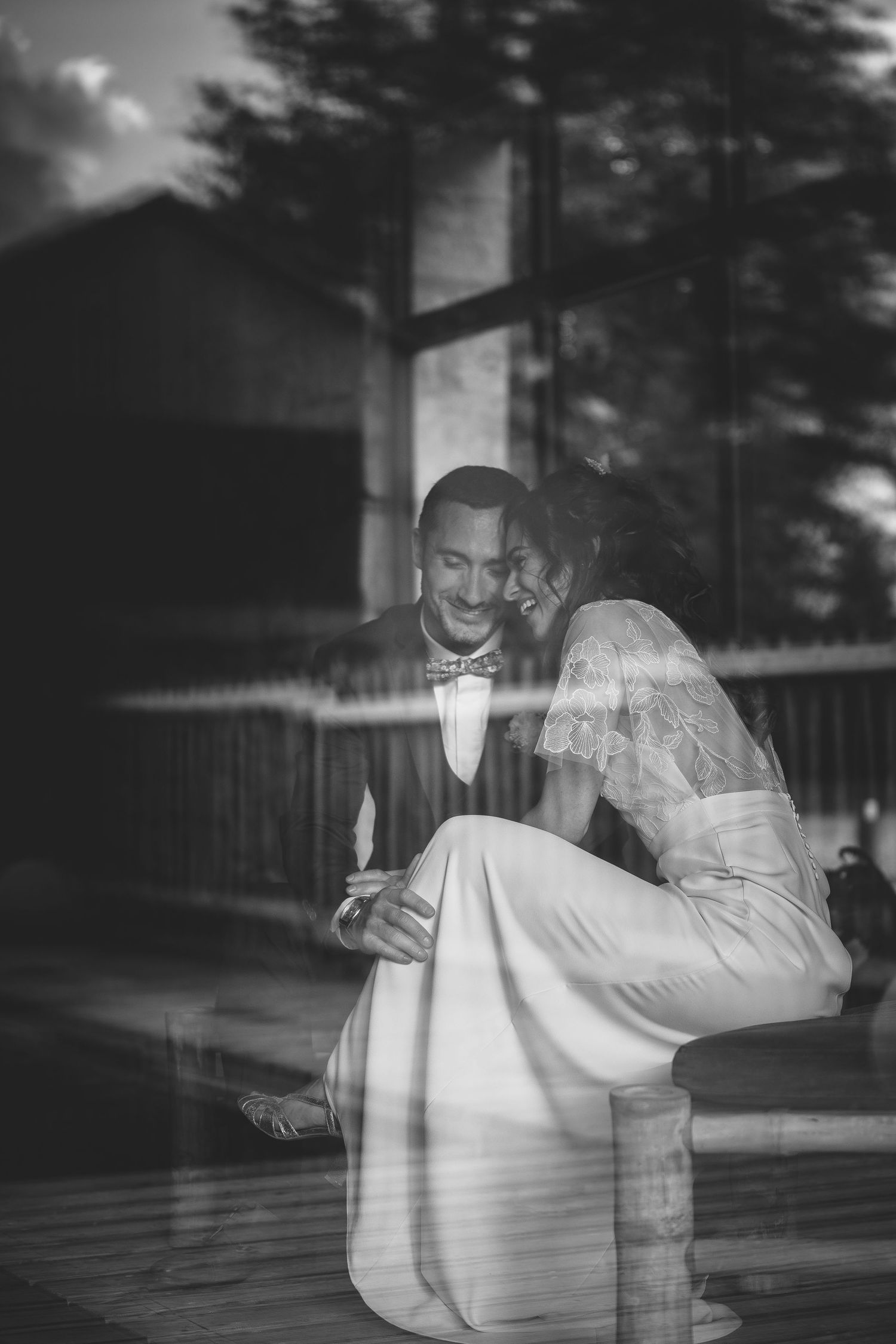 Black and white reflection of couple embracing through window glass.