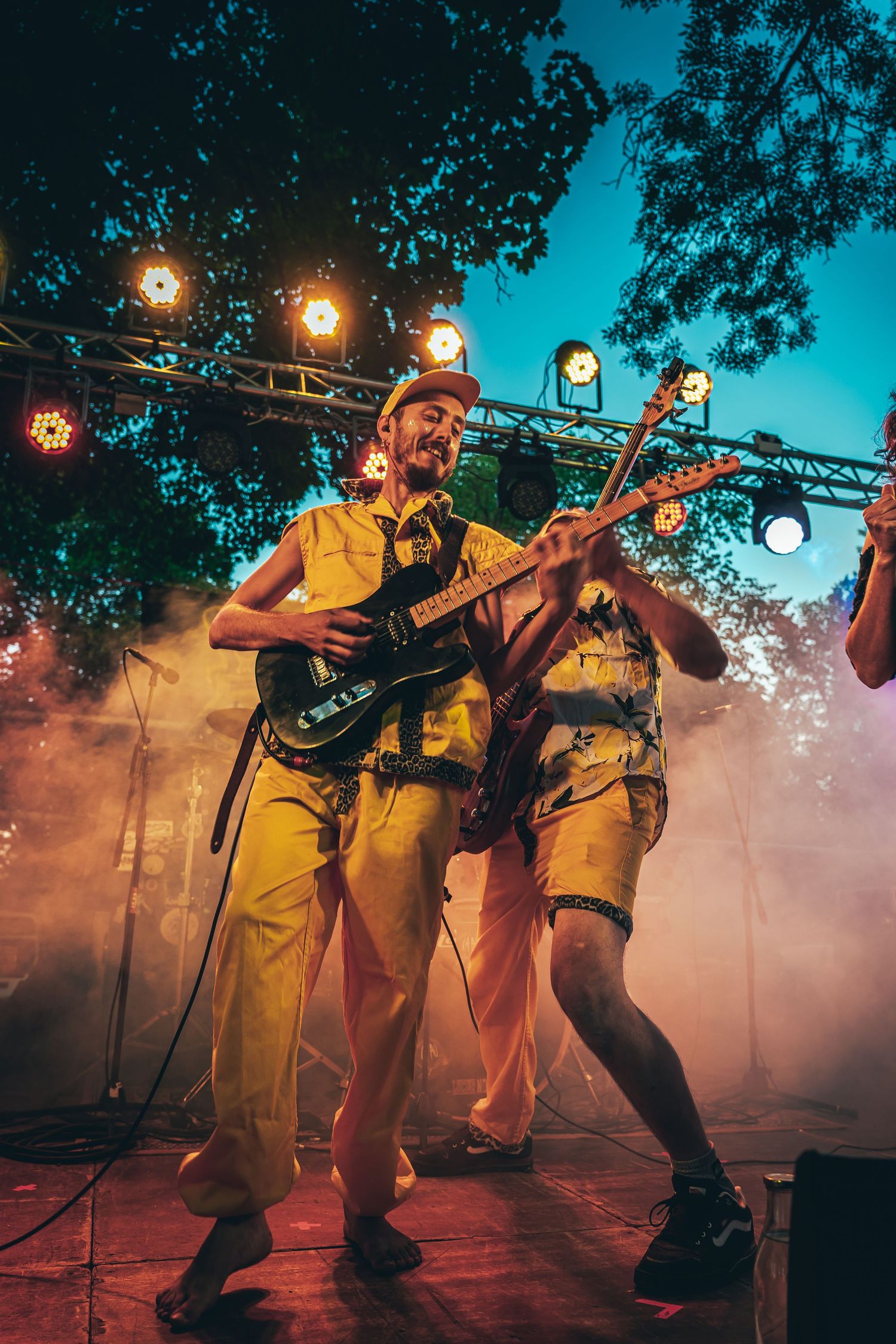 Band members in yellow uniforms performing energetically on stage with atmospheric lighting and fog effects.