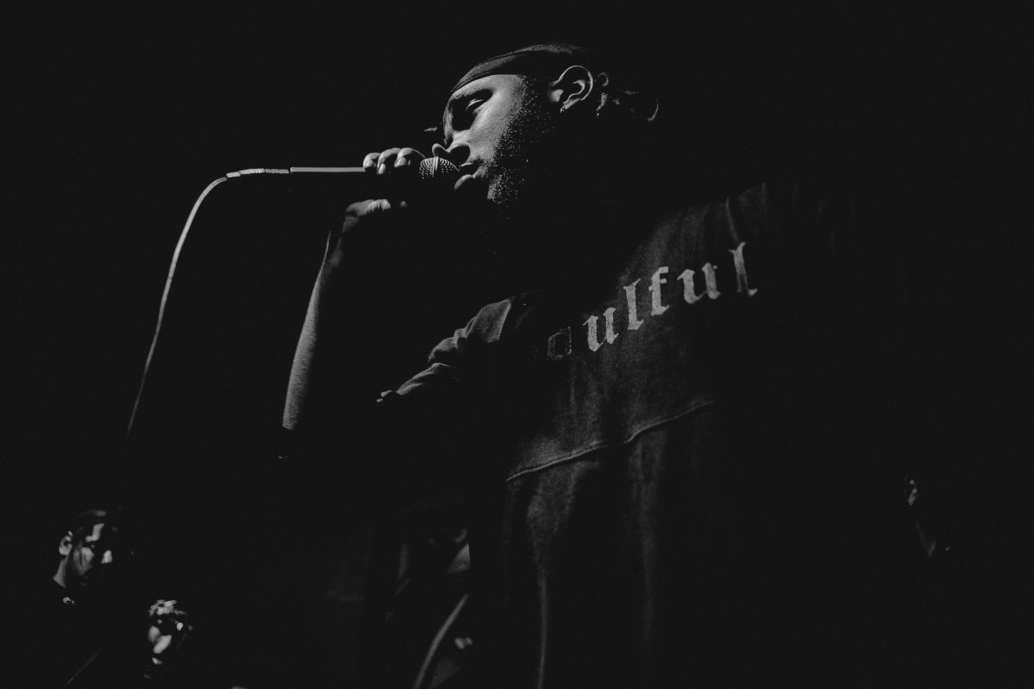 A dark concert stage with a guitarist performing in silhouette against dramatic lighting.