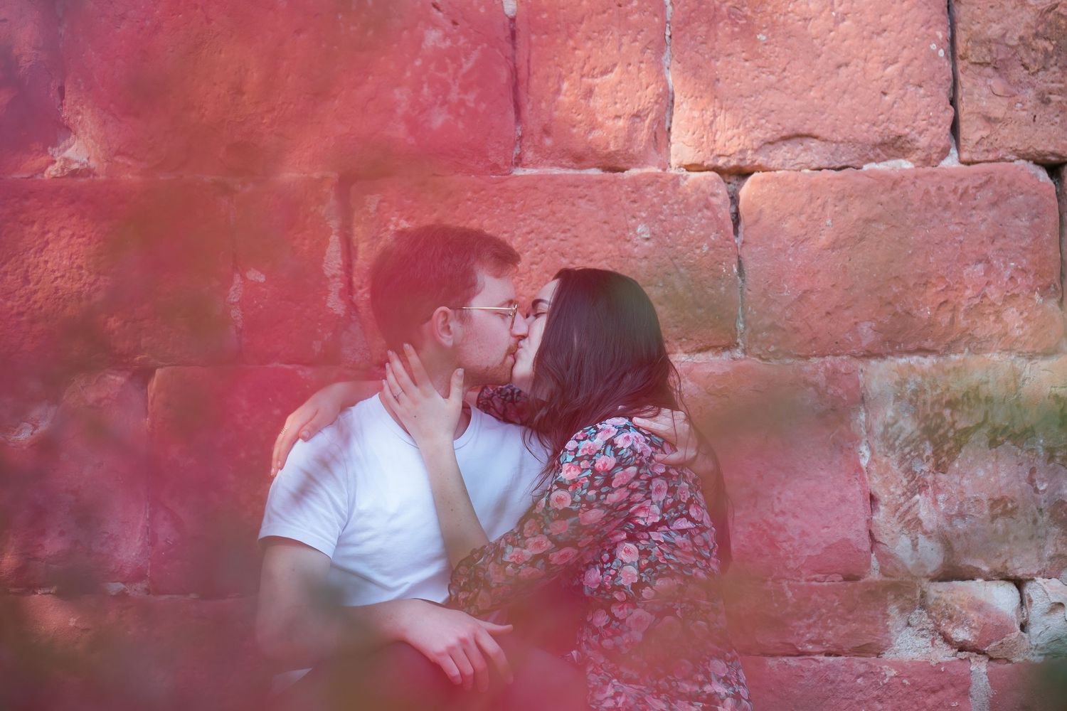 Intimate moment between couple against pink stone wall background.