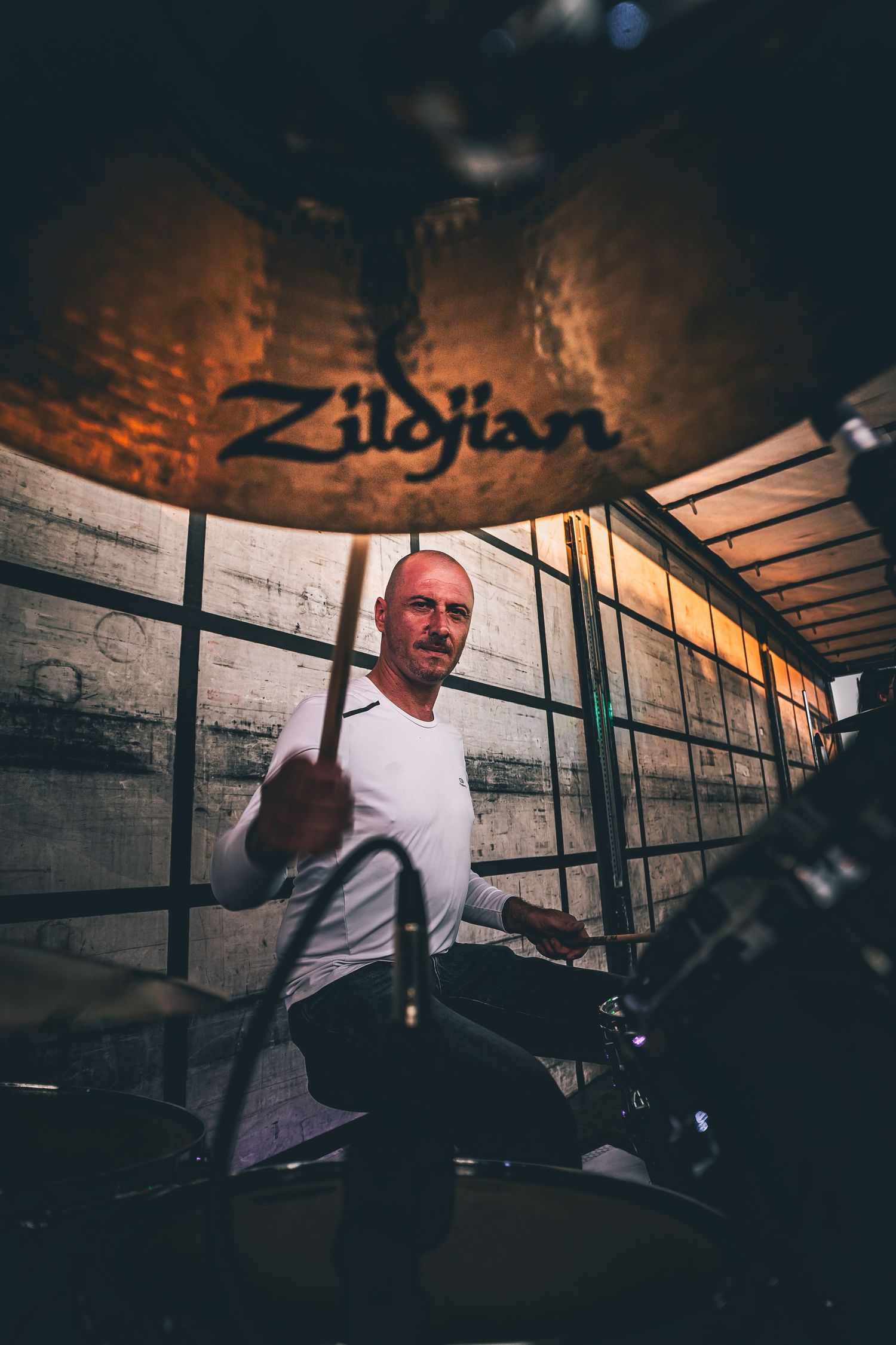 Drummer performing behind drum kit with Zildjian cymbal visible in moody lighting setup.