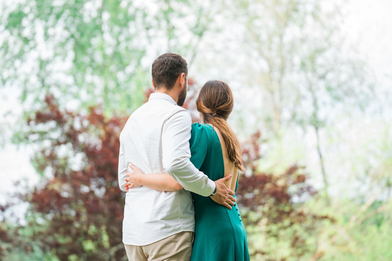 A couple in coordinated outfits embraces in a dreamy outdoor setting with soft natural lighting.