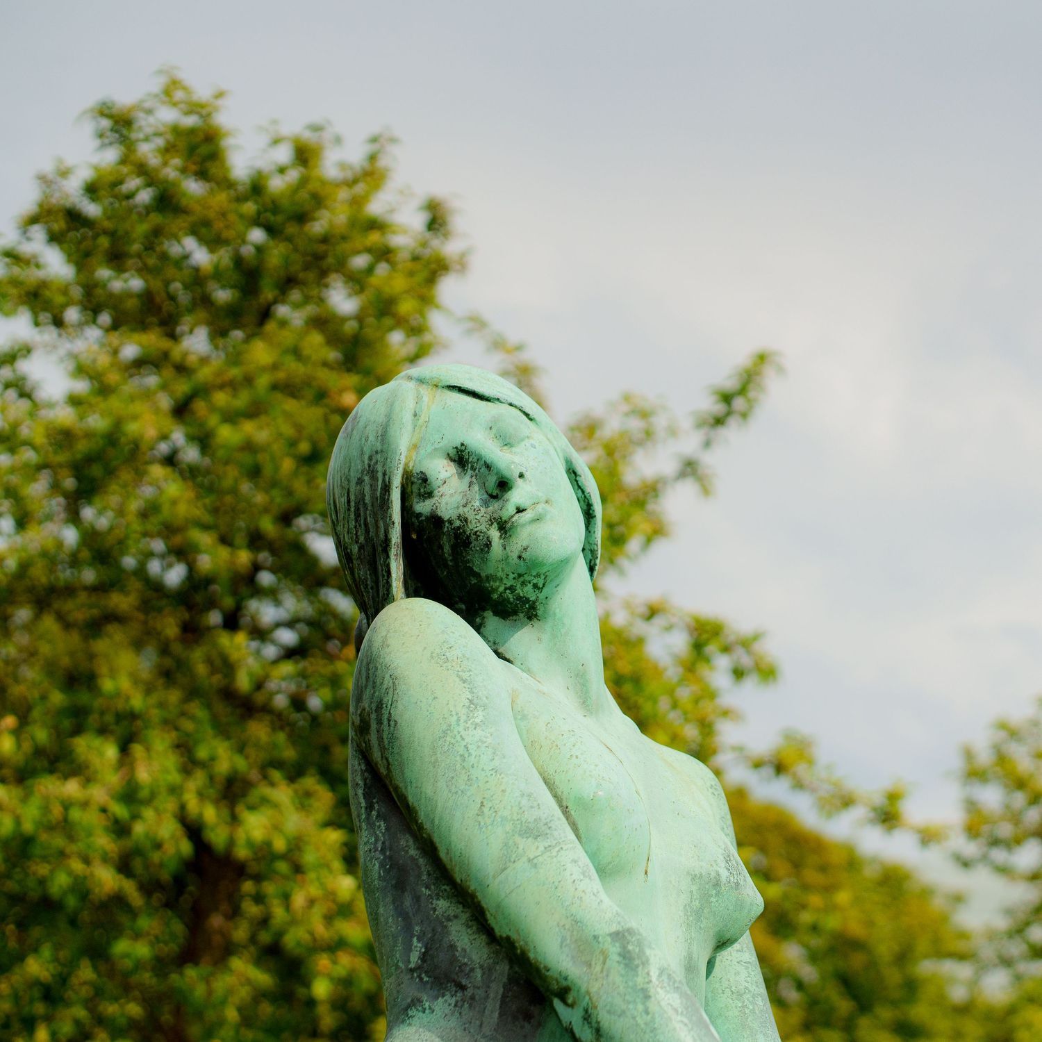 Green patinated bronze sculpture photographed against trees and sky.