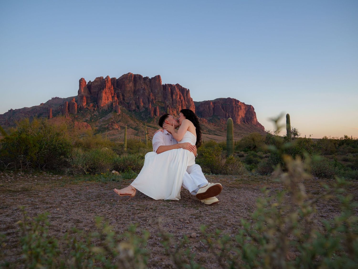 Desert engagement photo session with couple in formal attire against dramatic red rock formations at sunset in Arizona.