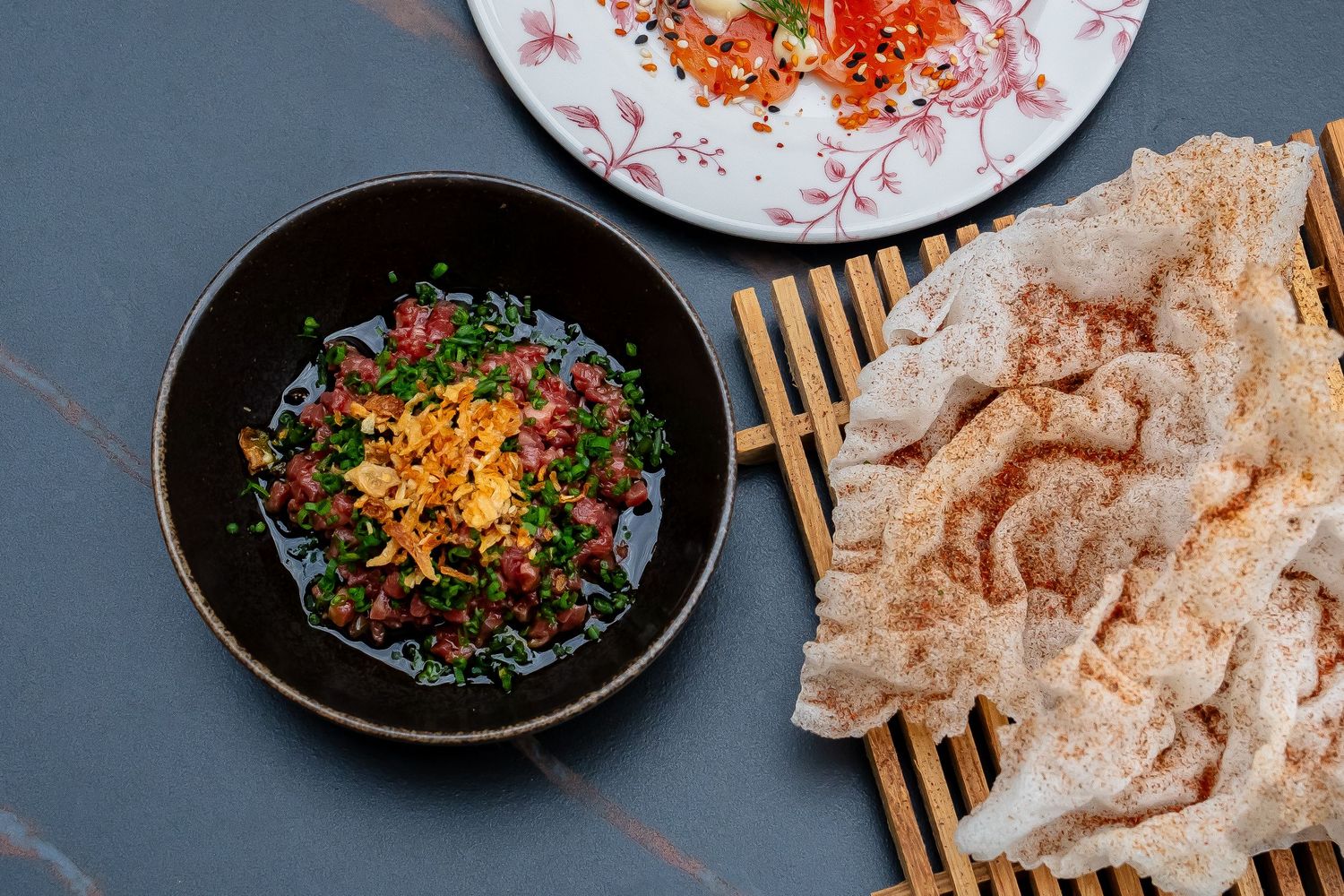 Colorful Asian cuisine dishes arranged on dark plates with garnishes.