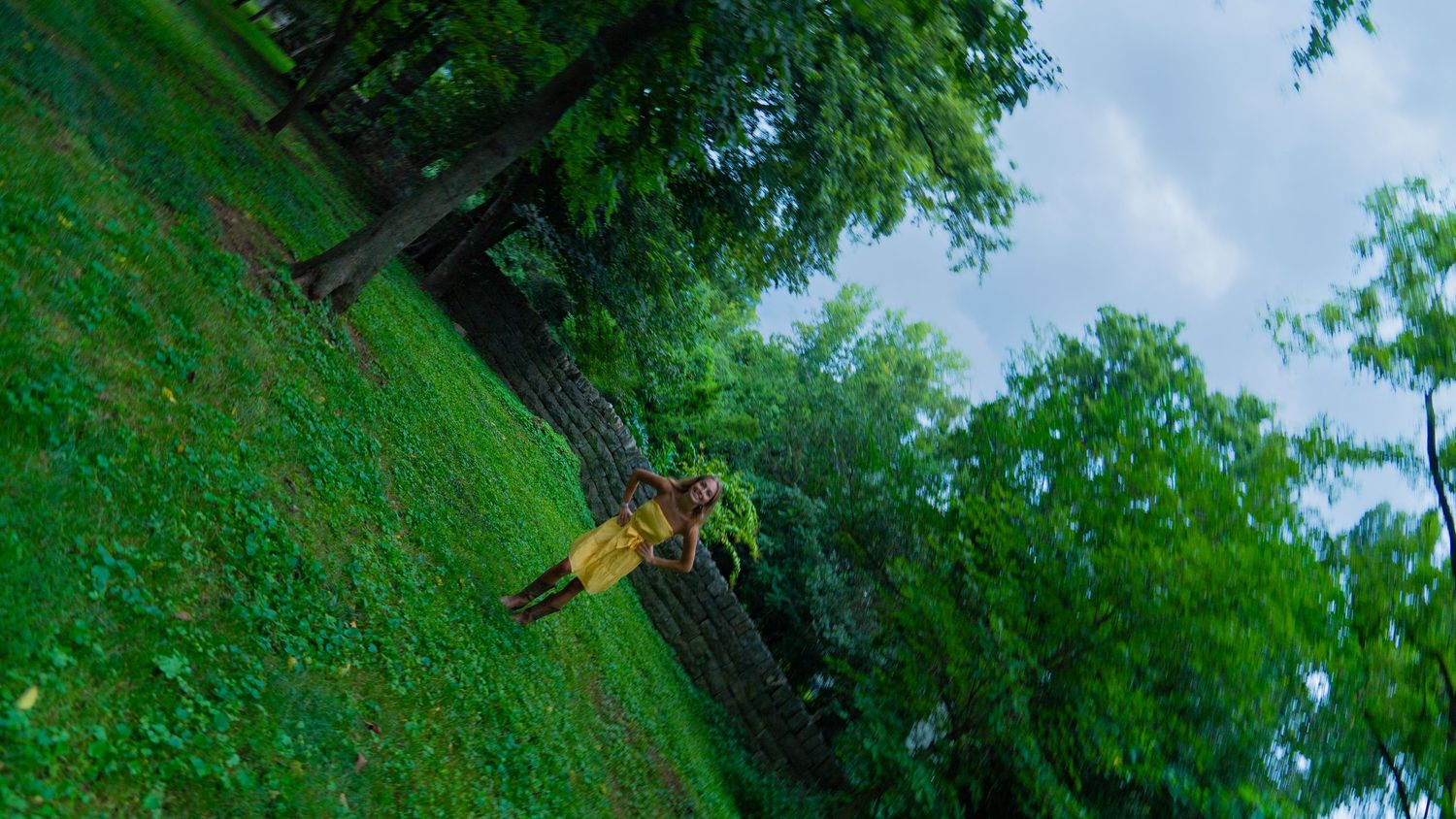 Girl in a yellow dress and verdant tree branches and leaves create natural frame against blue sky.