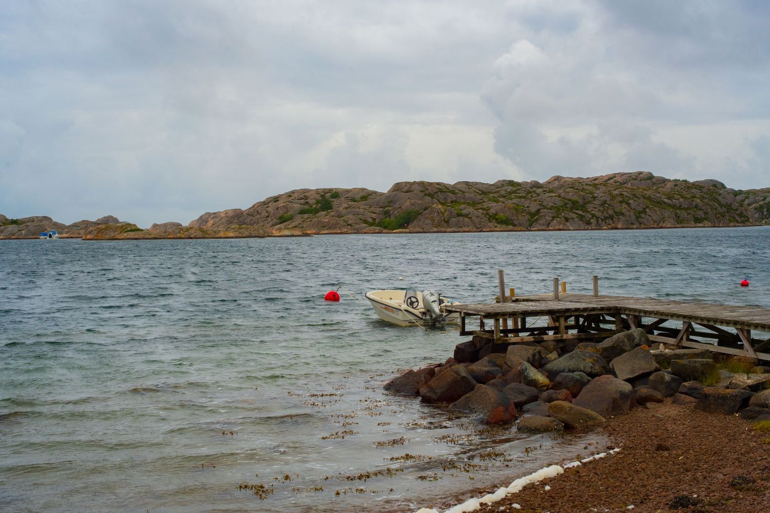 Scenic view of a rocky coastline with calm waters and small boats moored along the shore during overcast weather.