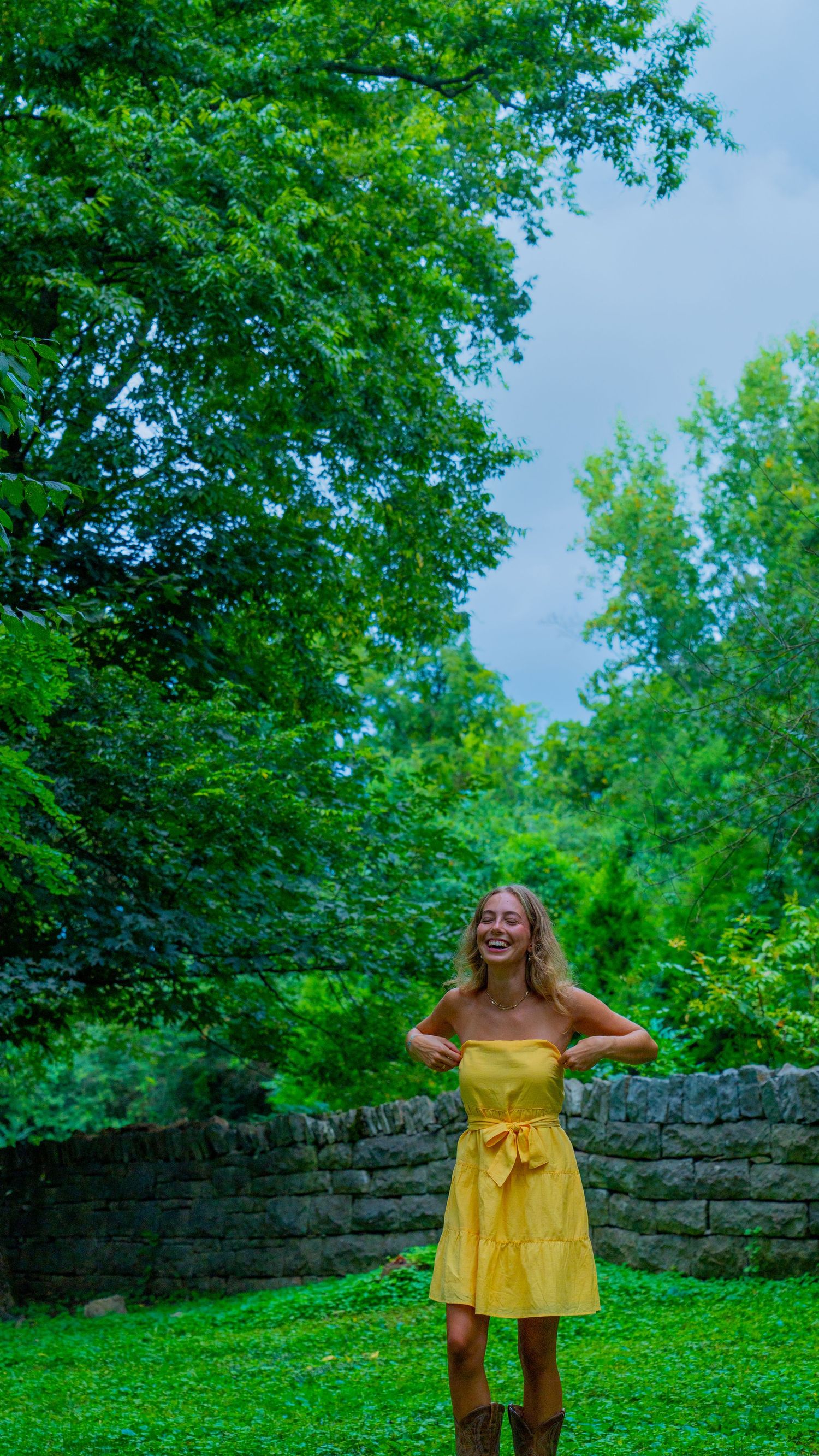 Yellow sundress against lush green garden and stone wall backdrop.