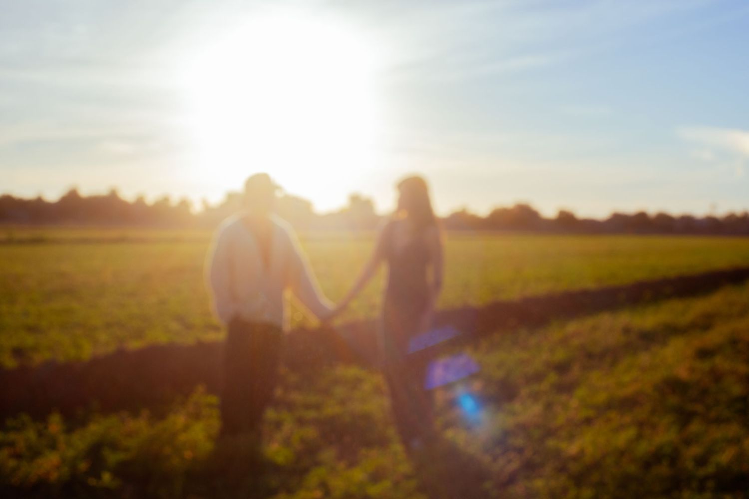 Silhouetted figures stand in a golden sunlit field during a beautiful sunset creating a dreamy atmosphere.