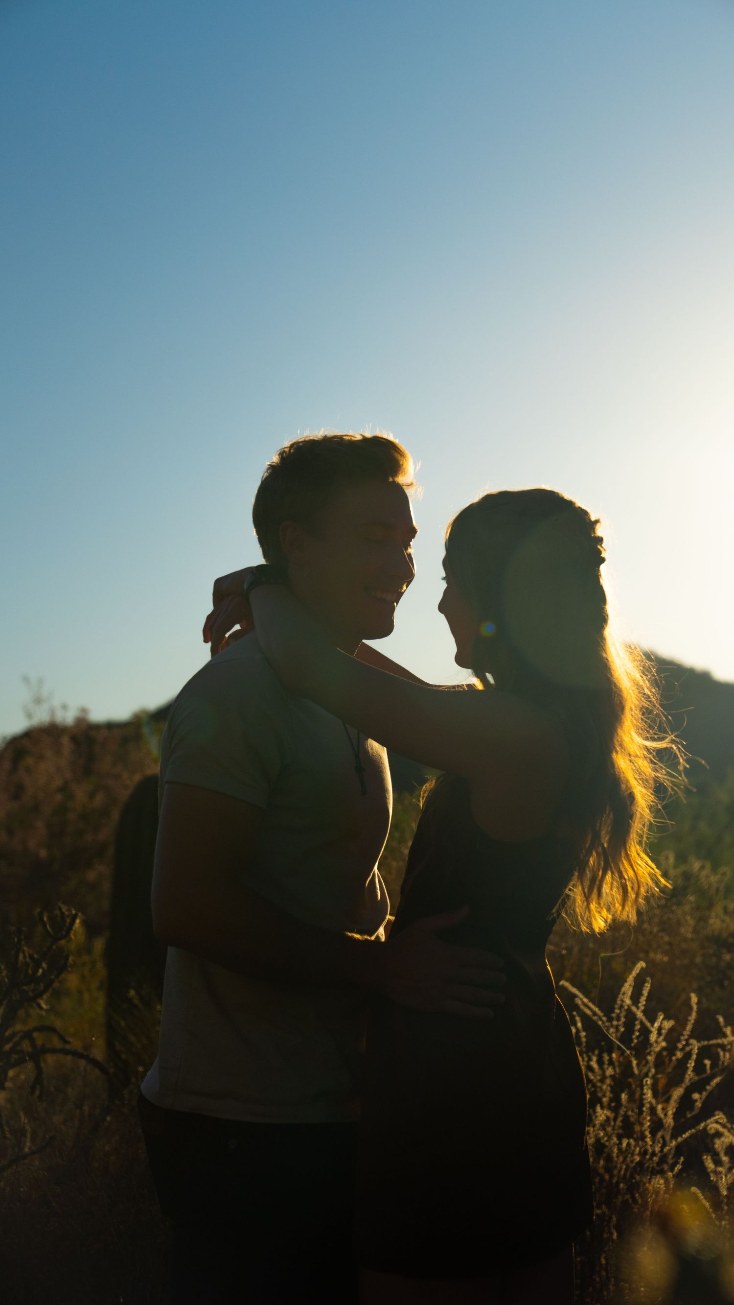 Silhouetted couple sharing an intimate moment at sunset against a soft blue sky.