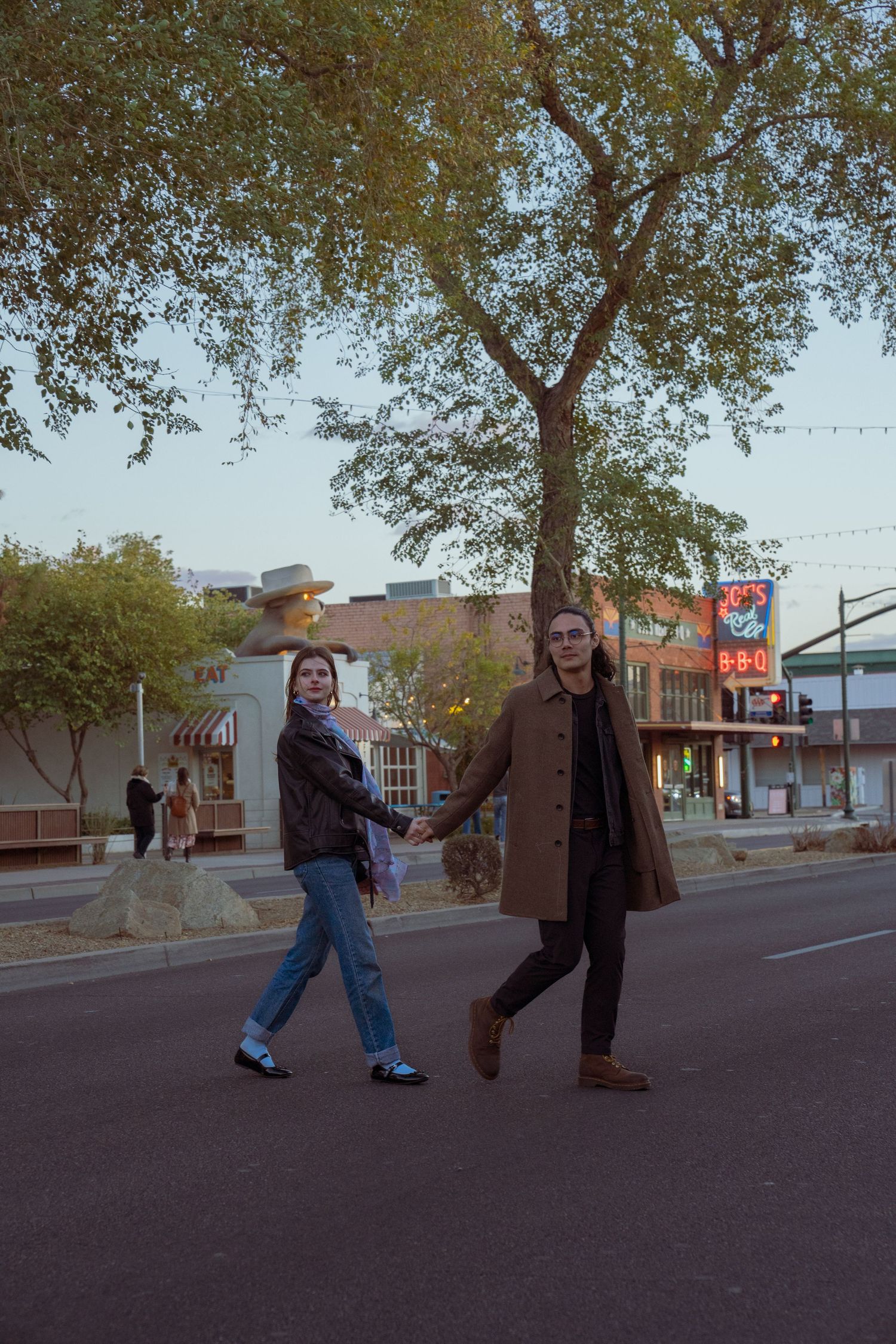 People walking down a small town street lined with trees and storefronts.
