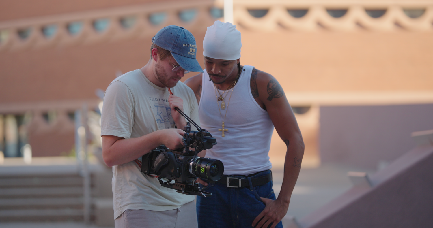 Two men reviewing footage on a professional camera outdoors on a sunny day.