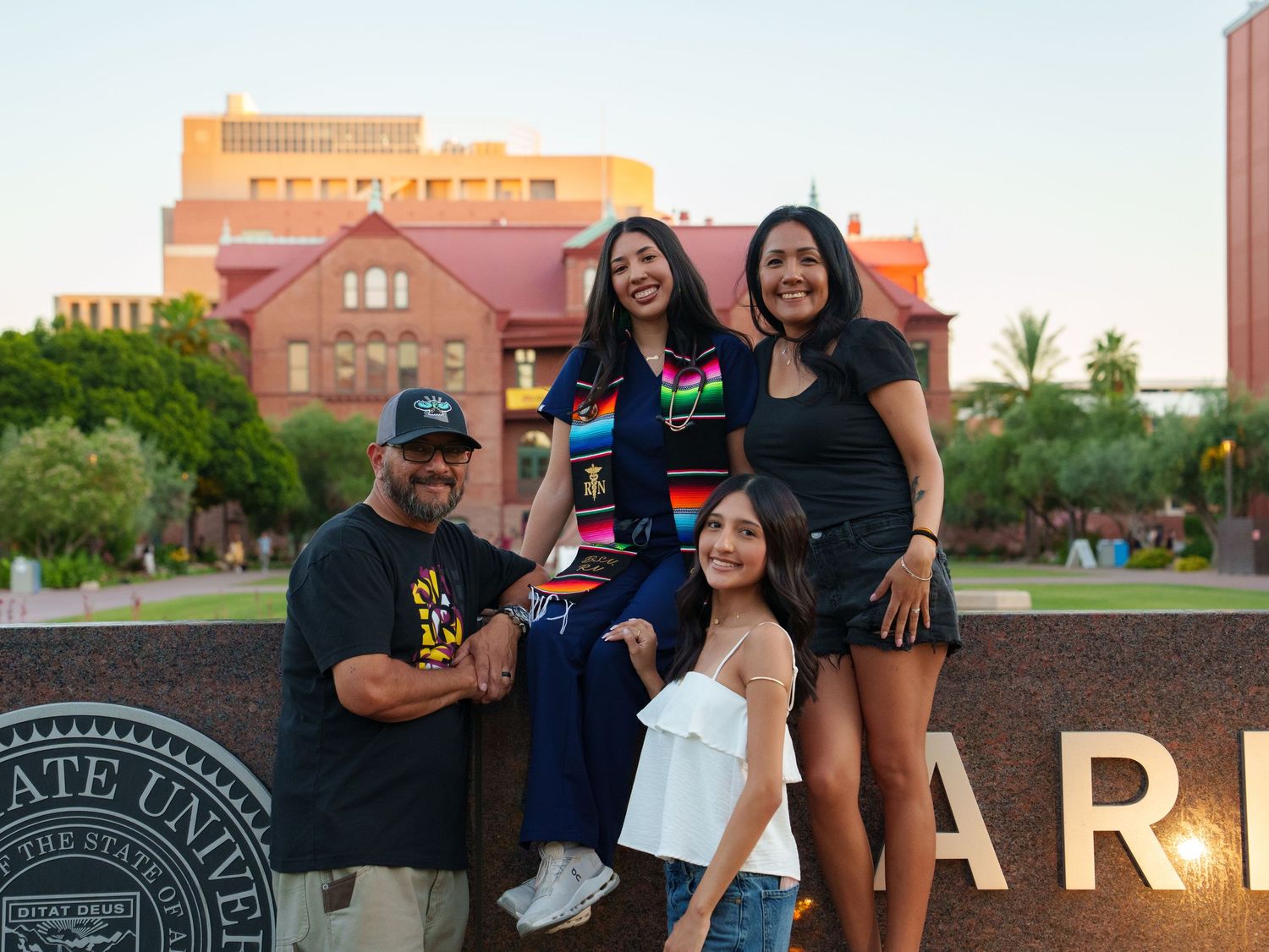 Family of four posing together in front of Arizona State University sign on a sunny day.