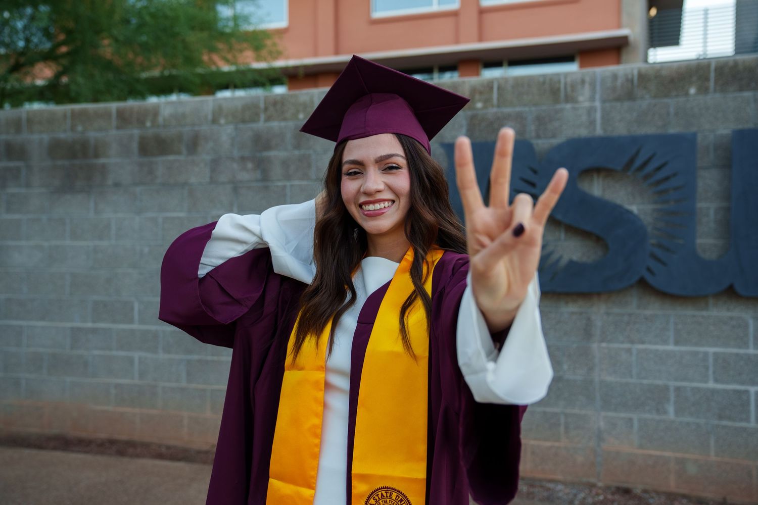 Graduate wearing purple cap and gown with yellow stole celebrating graduation outdoors.