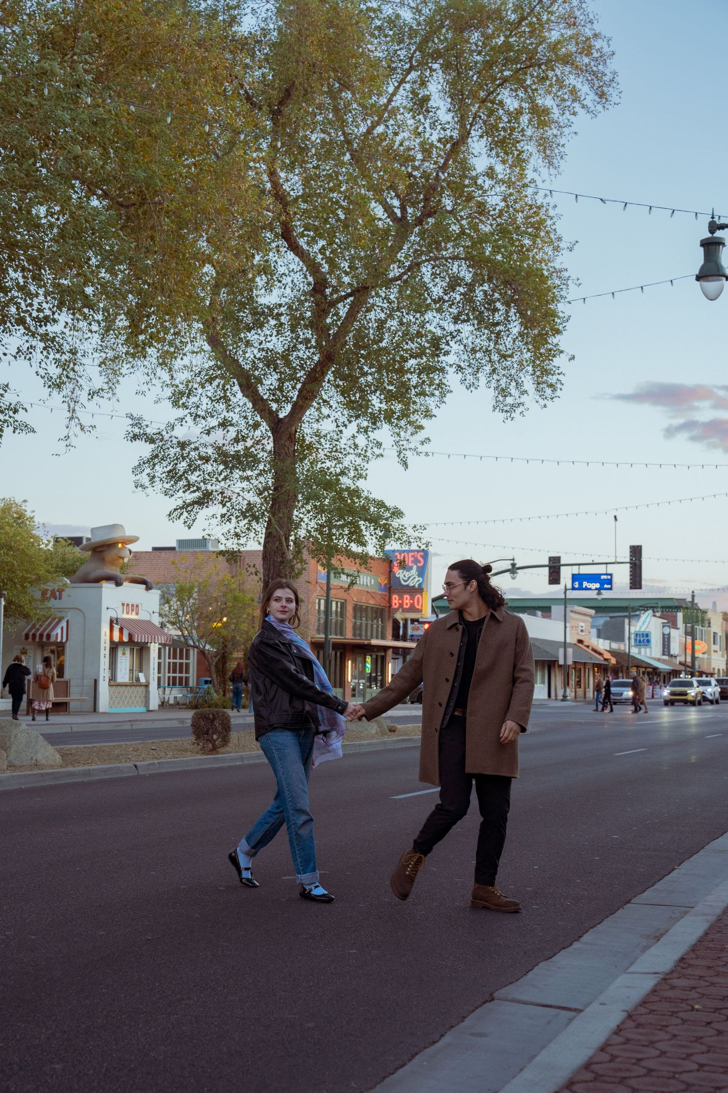 Couple walking along a small town street with trees and storefronts in the background.