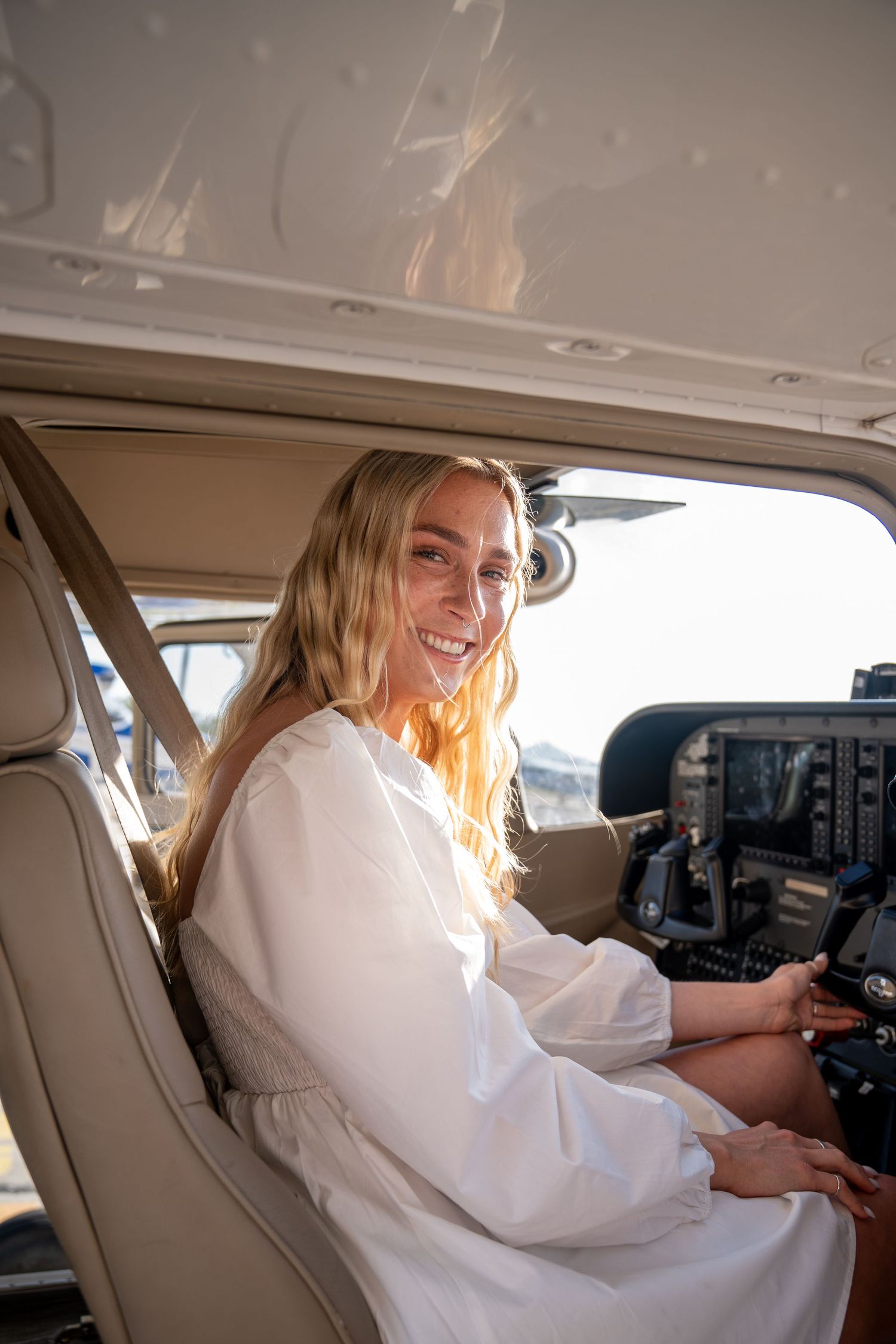 Person in white dress sitting in aircraft cockpit operating controls and instruments during flight.