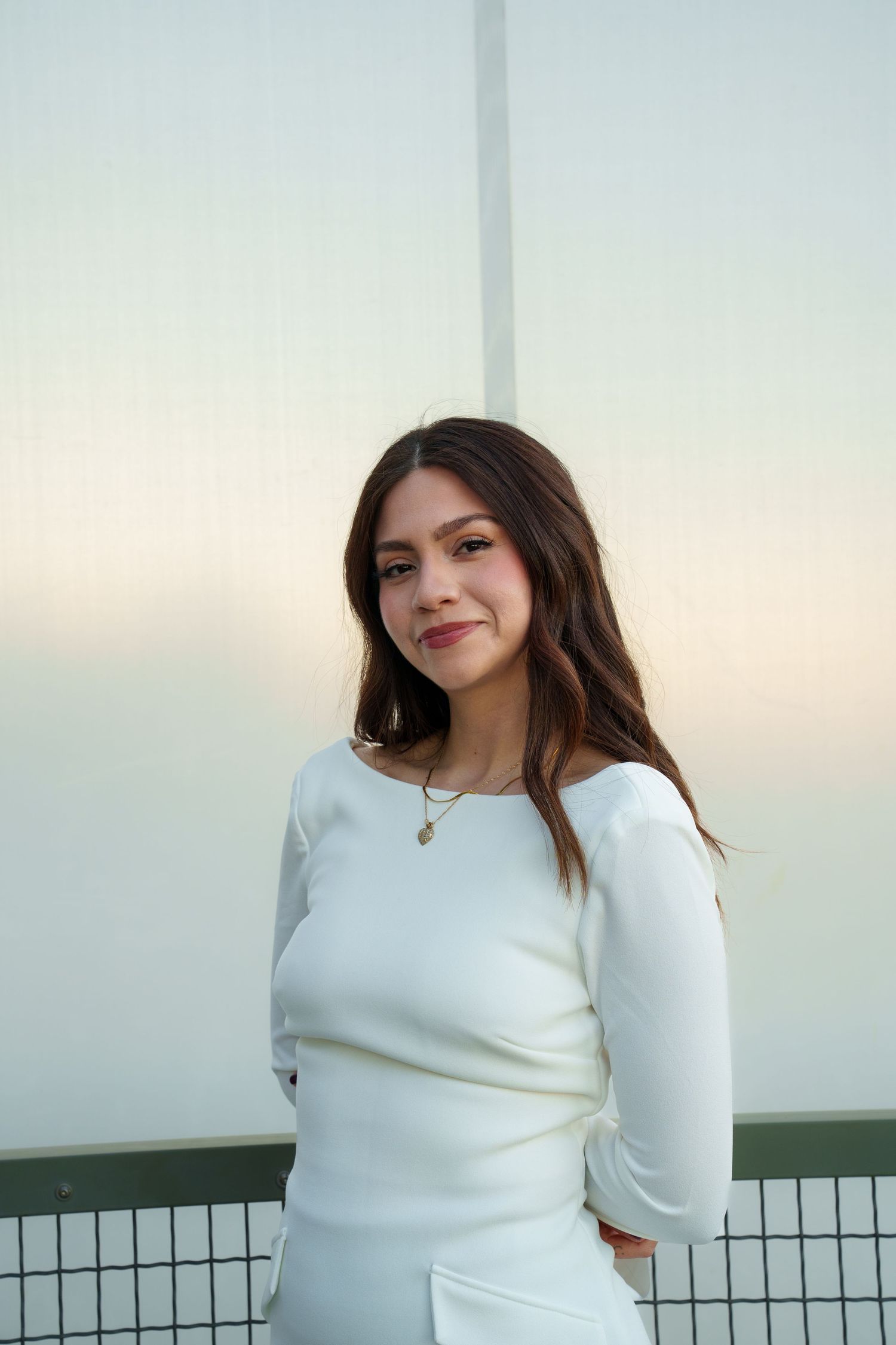 Person in a white sweater poses outdoors against a railing during golden hour.
