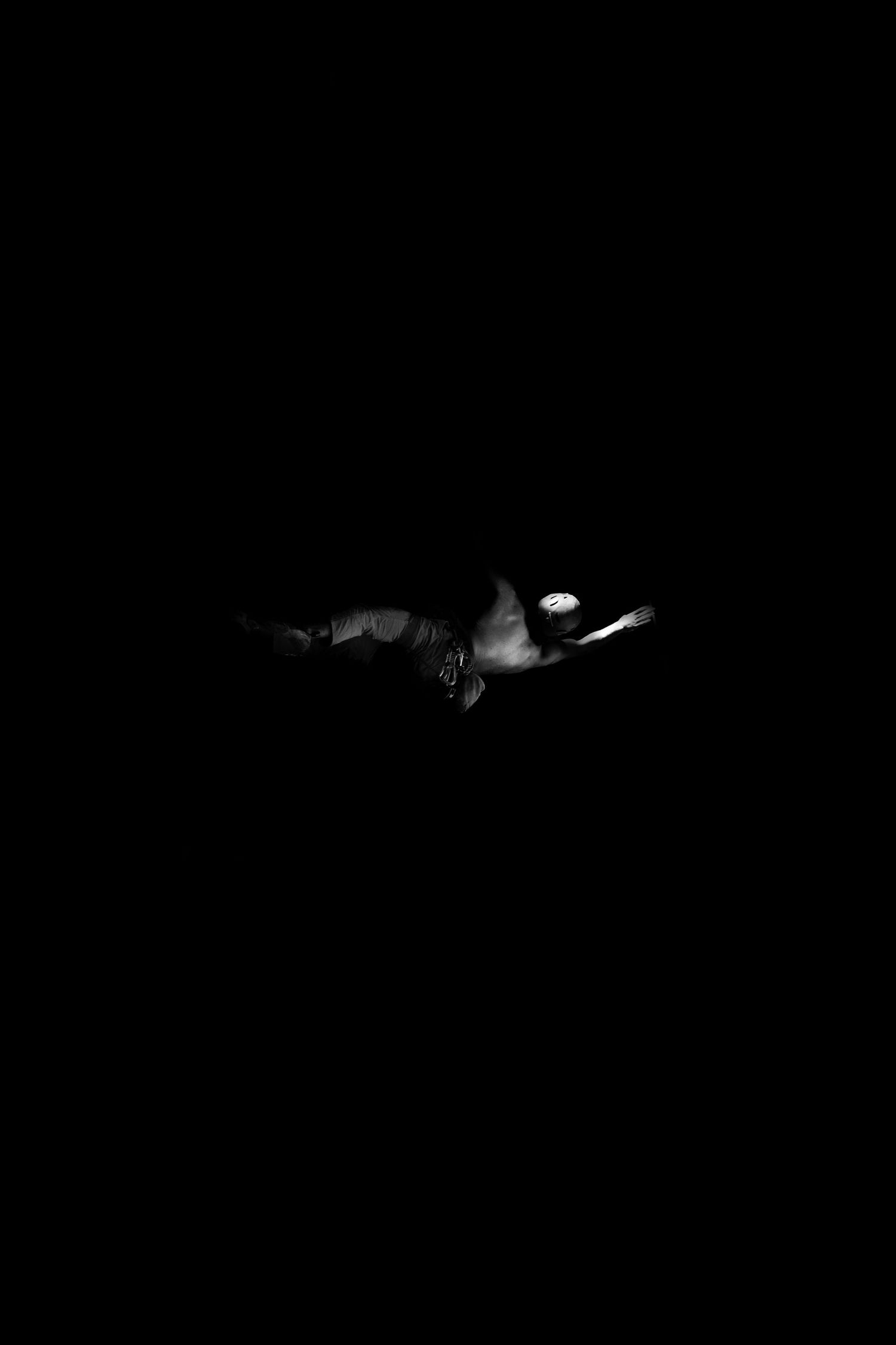 Rock climber in a dark atmospheric scene with subtle lighting effects in black background.