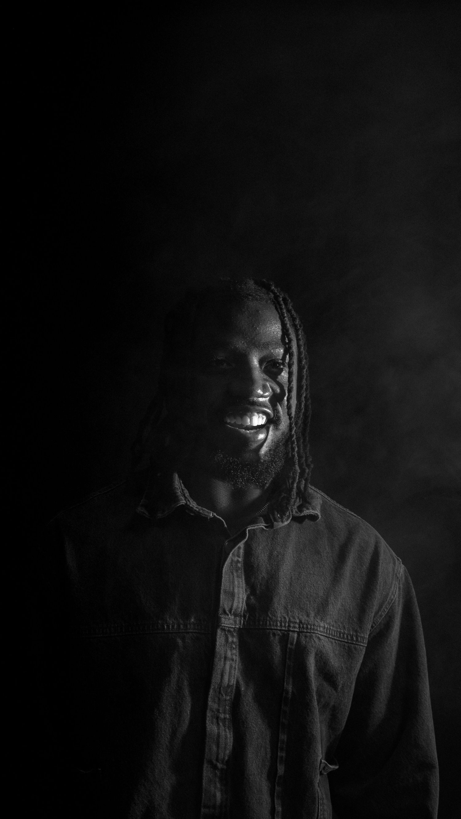 Dramatic low-key portrait in black and white with moody lighting and shadows.