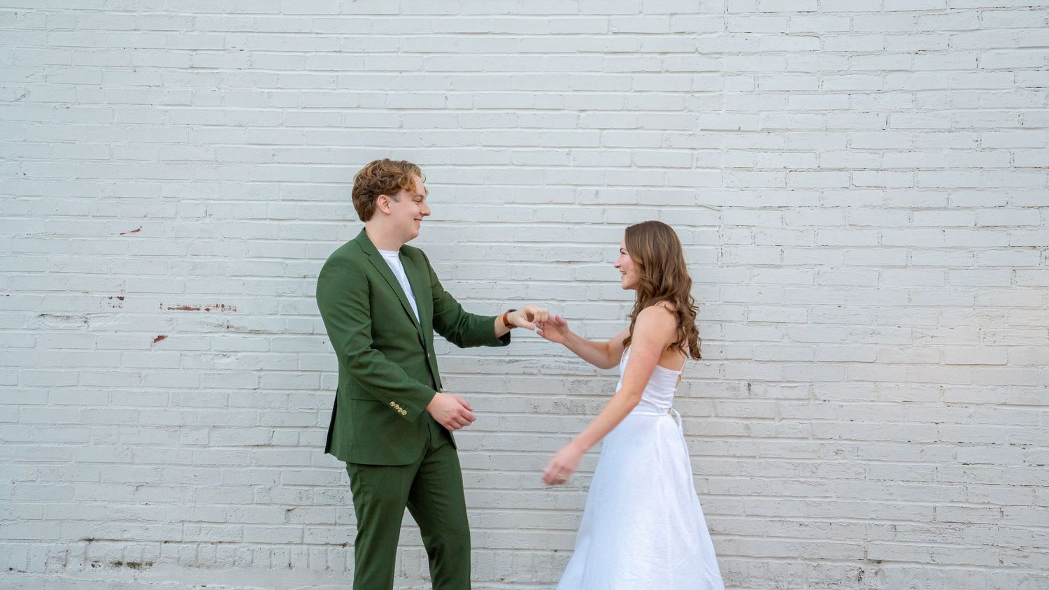 Couple strikes fun poses against white brick wall showing progression of dance-like movements.