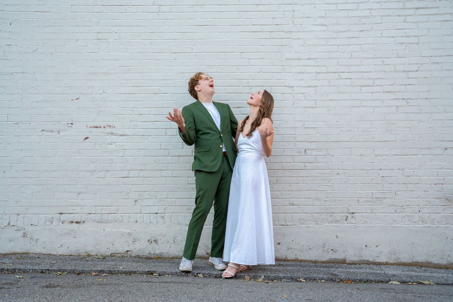 A playful couple in white dress and green suit pose against a white brick wall in a creative photo sequence.