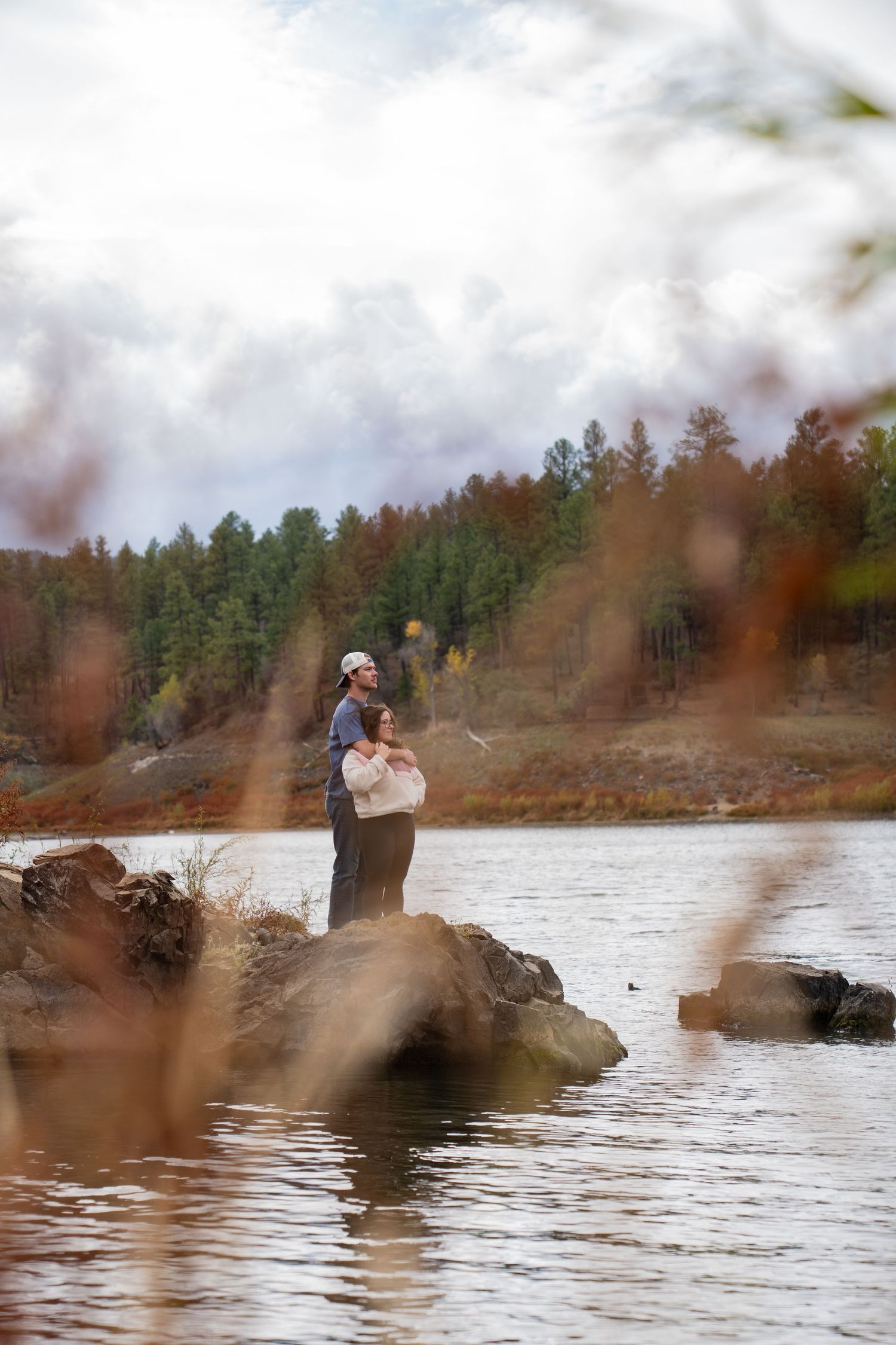 People enjoying a scenic lakeside view from a rocky outcrop on a cloudy day.