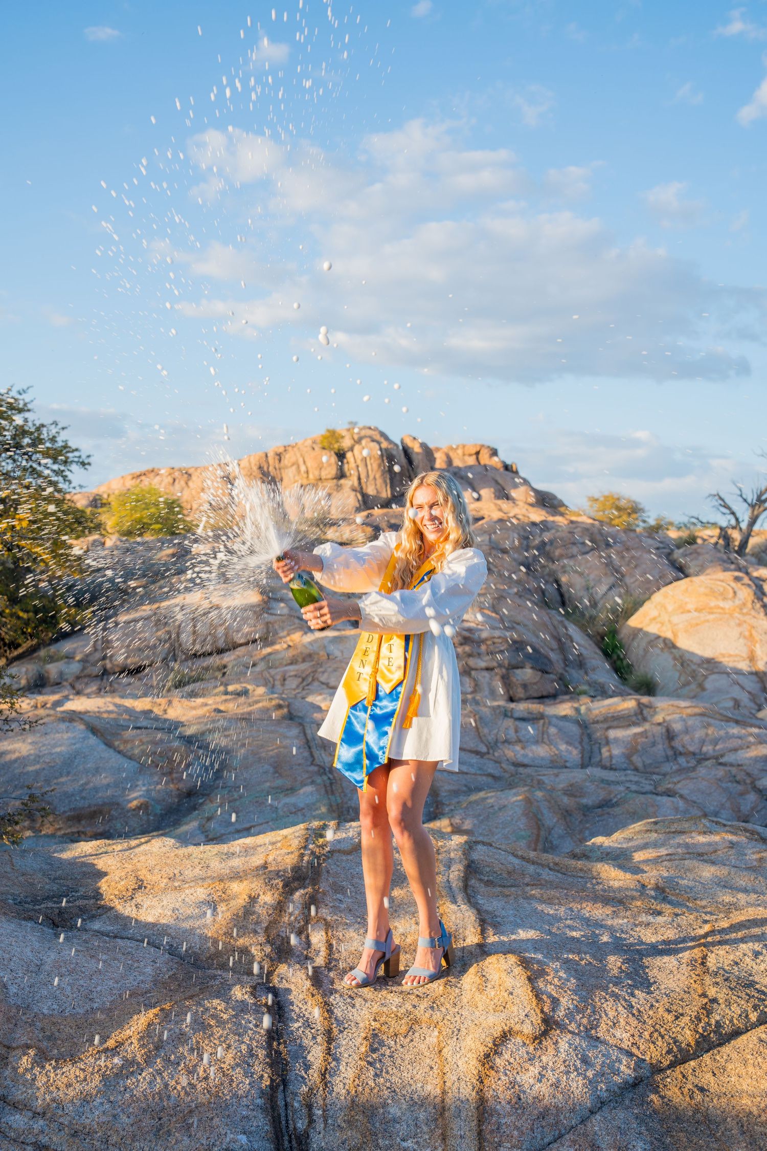 A couple plays in water splashes on rocky terrain at sunset while enjoying a fun outdoor moment together.