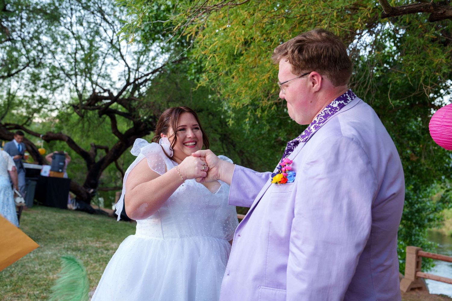 A couple in formal wedding attire dances together outdoors surrounded by trees and natural scenery.
