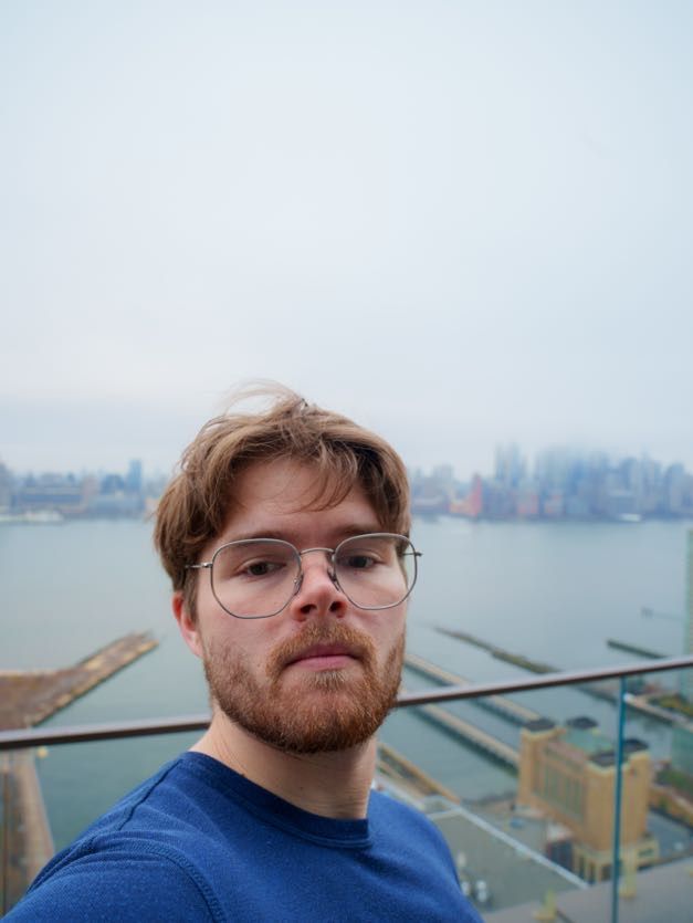 A selfie taken from a high vantage point overlooking a waterfront cityscape with buildings and piers visible in the background.