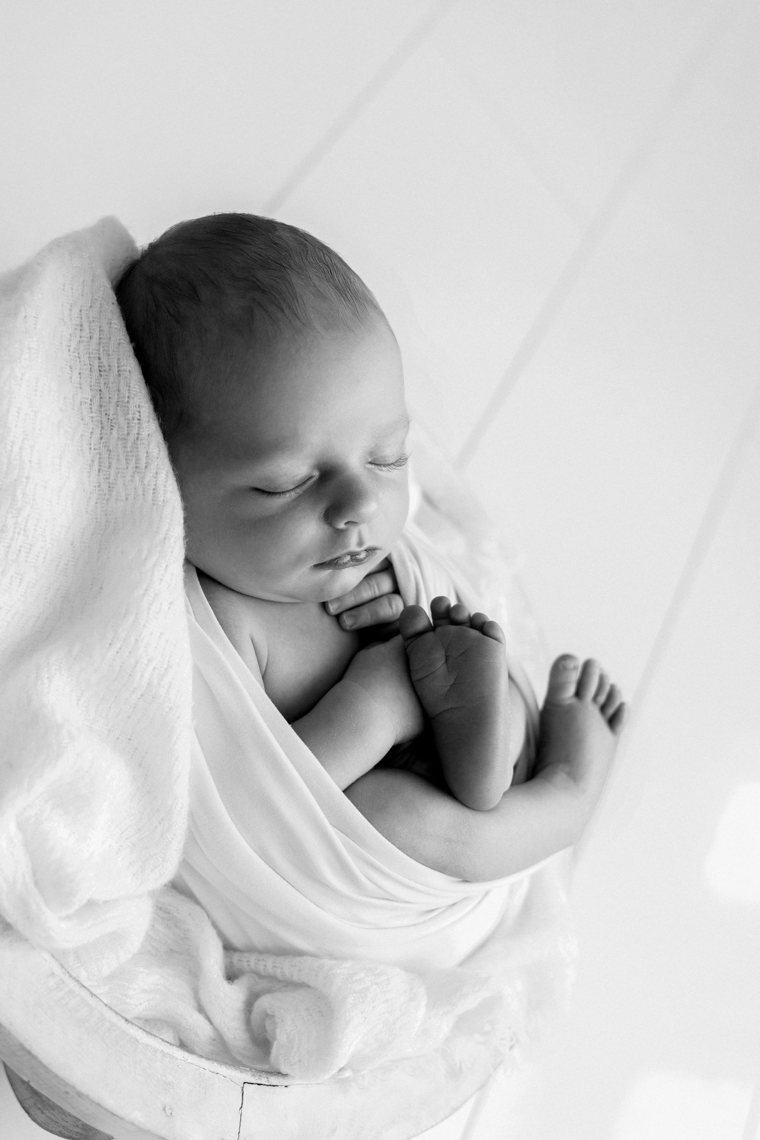 Black and white portrait of peaceful sleeping newborn baby wrapped in soft white blanket in bowl. Albury Wodonga Newborn Photographer