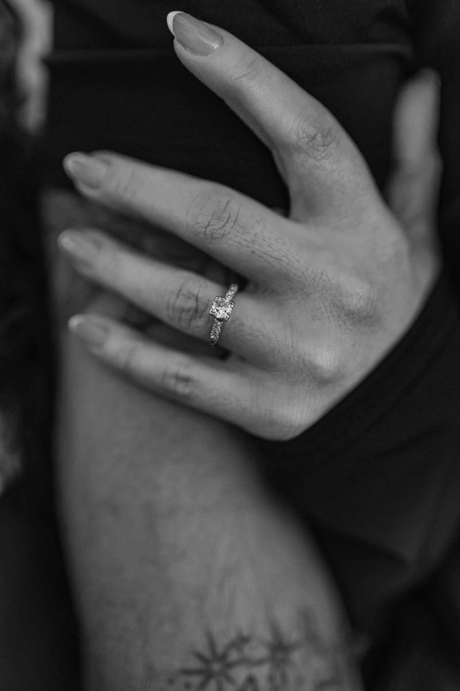 Close-up of a woman’s hand with manicured nails and an engagement ring gently resting on a man’s bicep, showcasing love and connection.