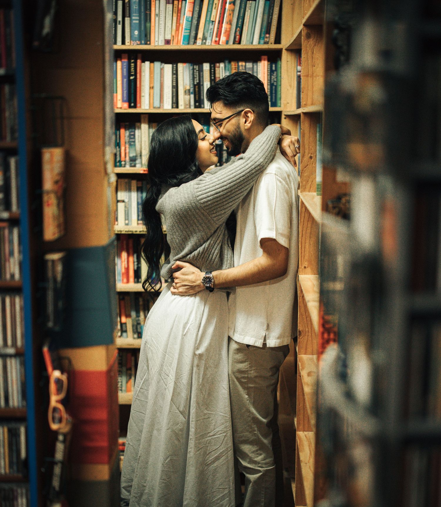 Couple embracing among bookshelves during pre-wedding photoshoot