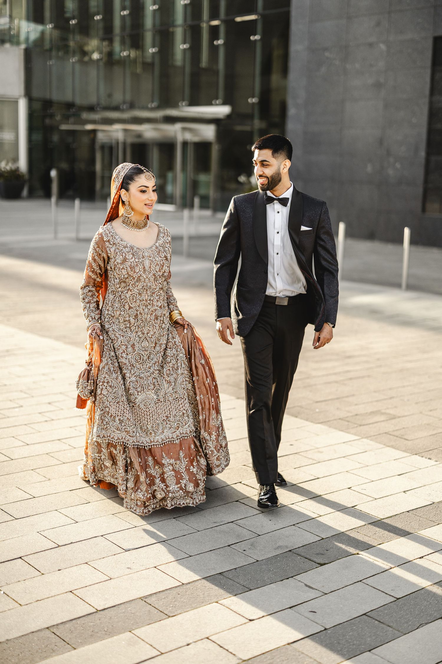 Bride and groom walking outdoors near modern architecture, reception portrait