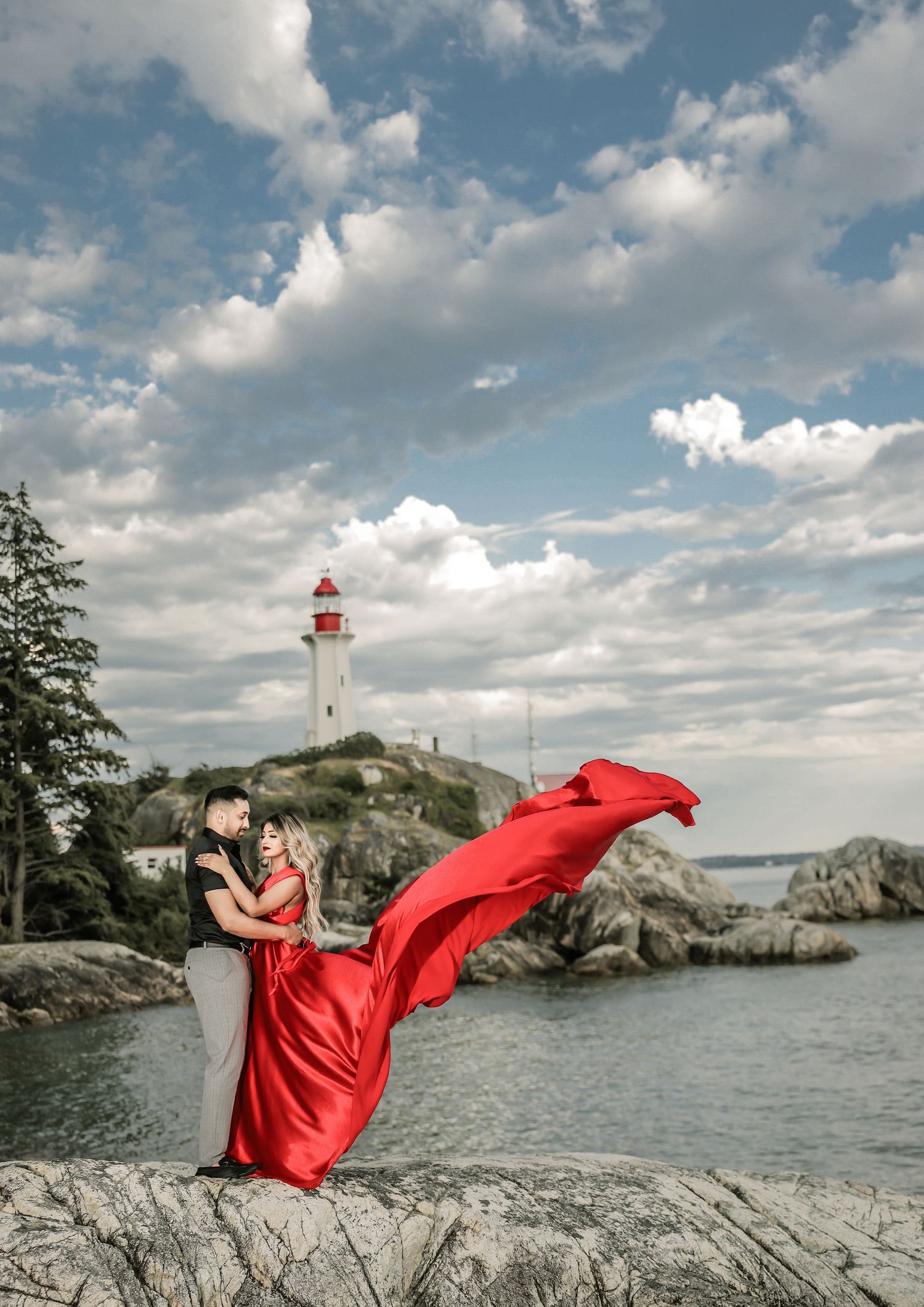 Bride in dramatic red gown on rocky shoreline, dramatic sky, pre-wedding portrait