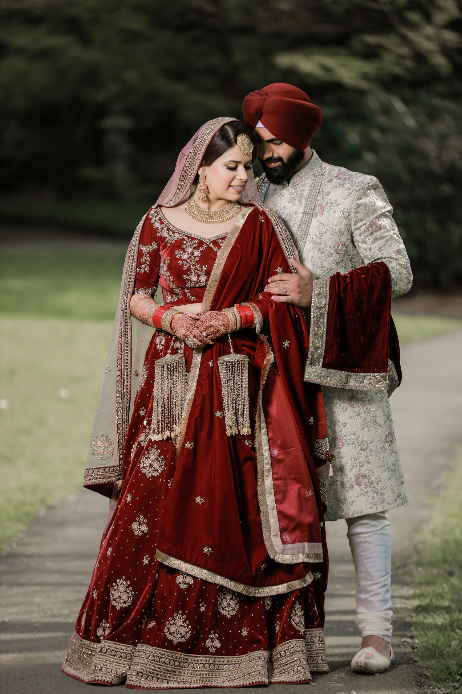 Sikh bride and groom in traditional red wedding attire, garden portrait