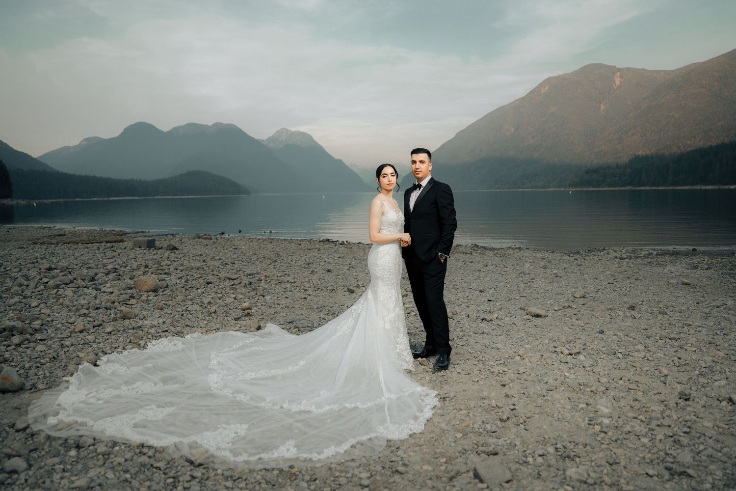 Bride and groom pre-wedding photoshoot on rocky beach with mountain backdrop, BC